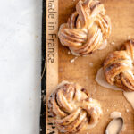 Image of freshly glazed espresso date knots/buns that have just been baked on a silicone baking mat on a baking sheet.