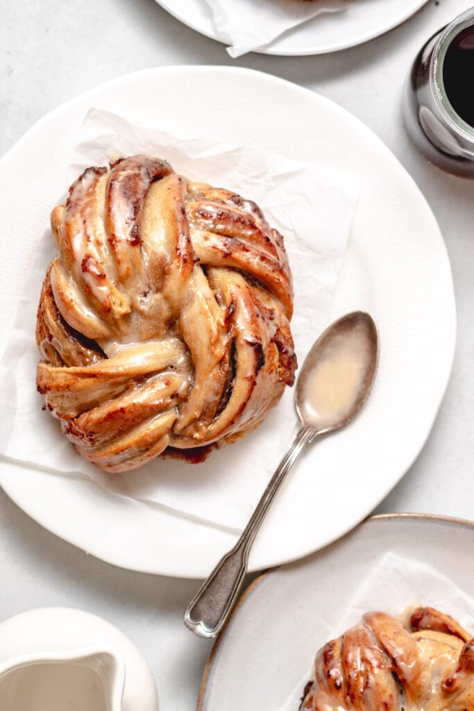 Image of a espresso date swirled breakfast bun on a piece of parchment paper on top of a plate.