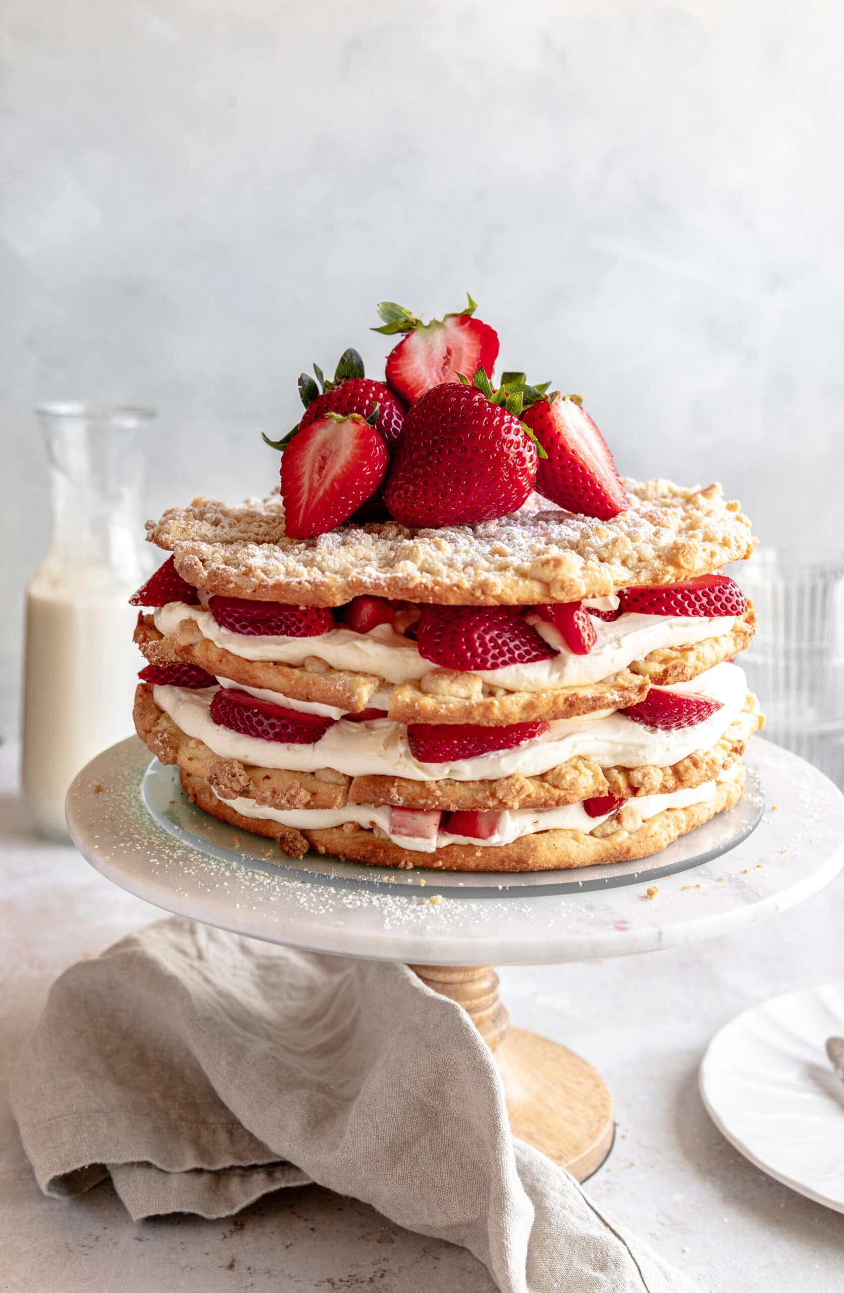 Image of a 4 tiered cake made from streusel cookie layers filled with strawberries and cream on a cake stand.
