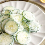 Up close of the gurken salat - cucumber salad - on a white plate layered on a neutral ceramic plate.