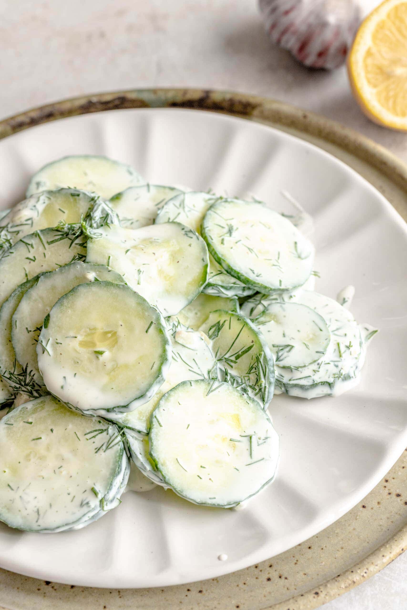 Up close of the gurken salat - cucumber salad - on a white plate layered on a neutral ceramic plate.