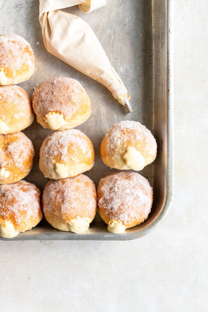 Vanillekrapfen lined up in a silver baking sheet with a piping bag.