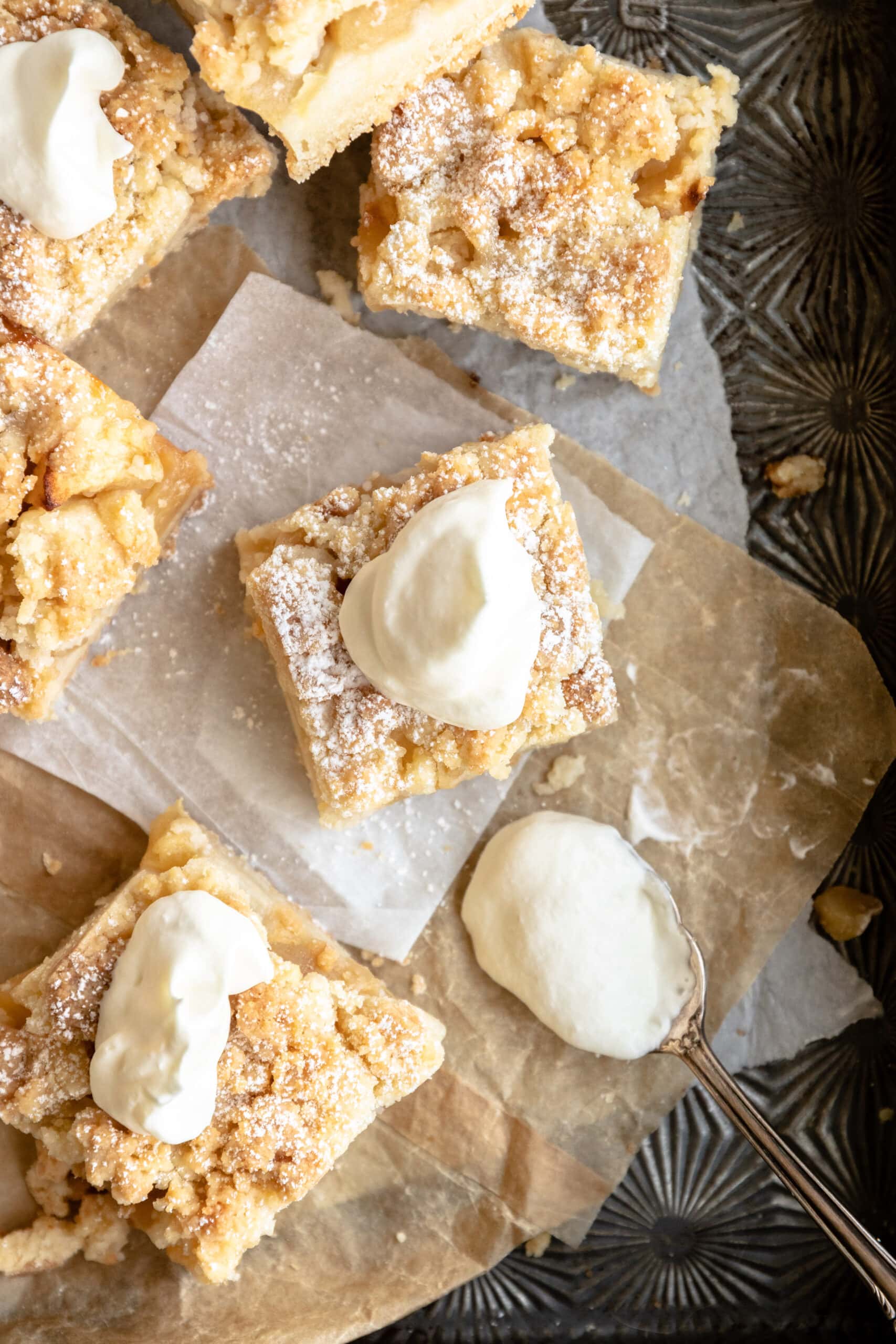 apfelstrueselkuchen bars on parchment and topped with whipped cream.