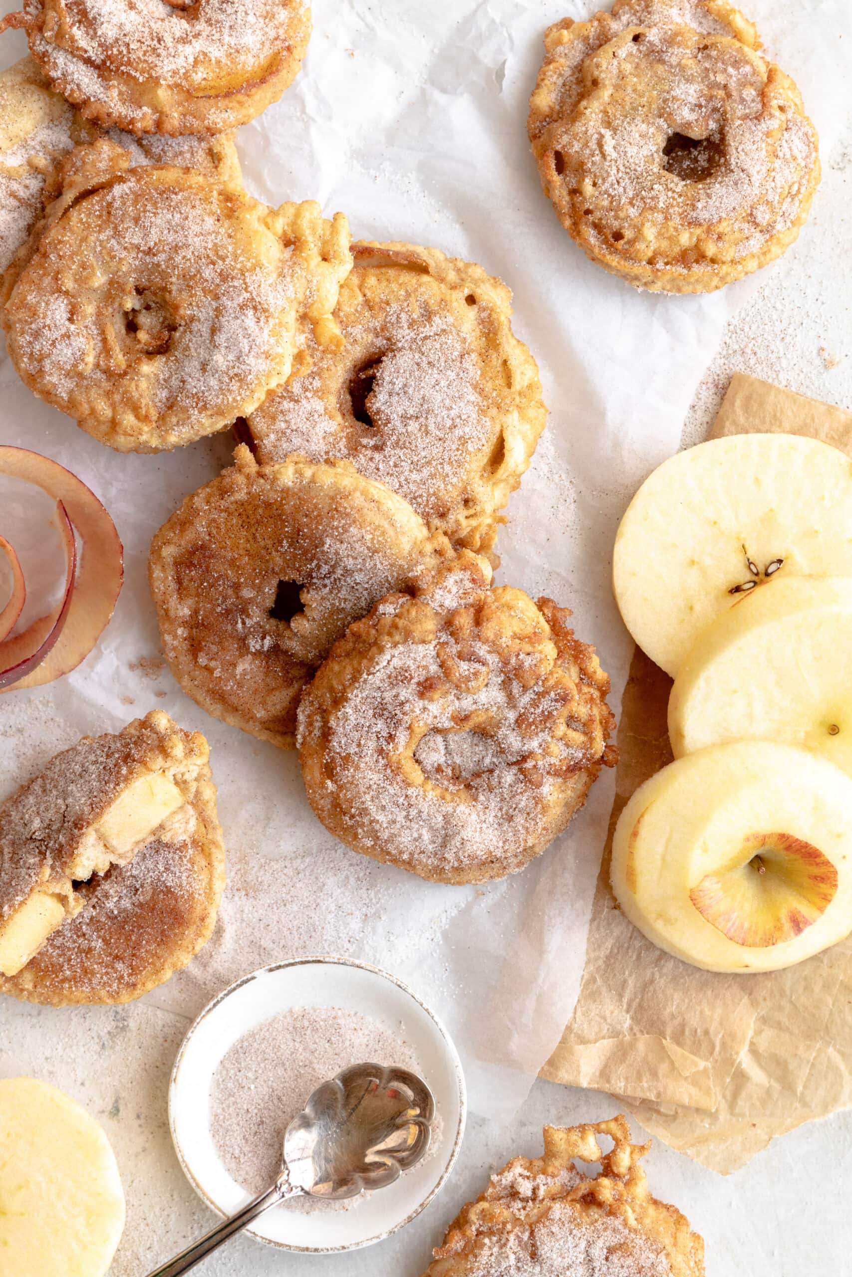 Overhead image of many fried apple rings coated in cinnamon sugar with a few slices of raw fresh apple.