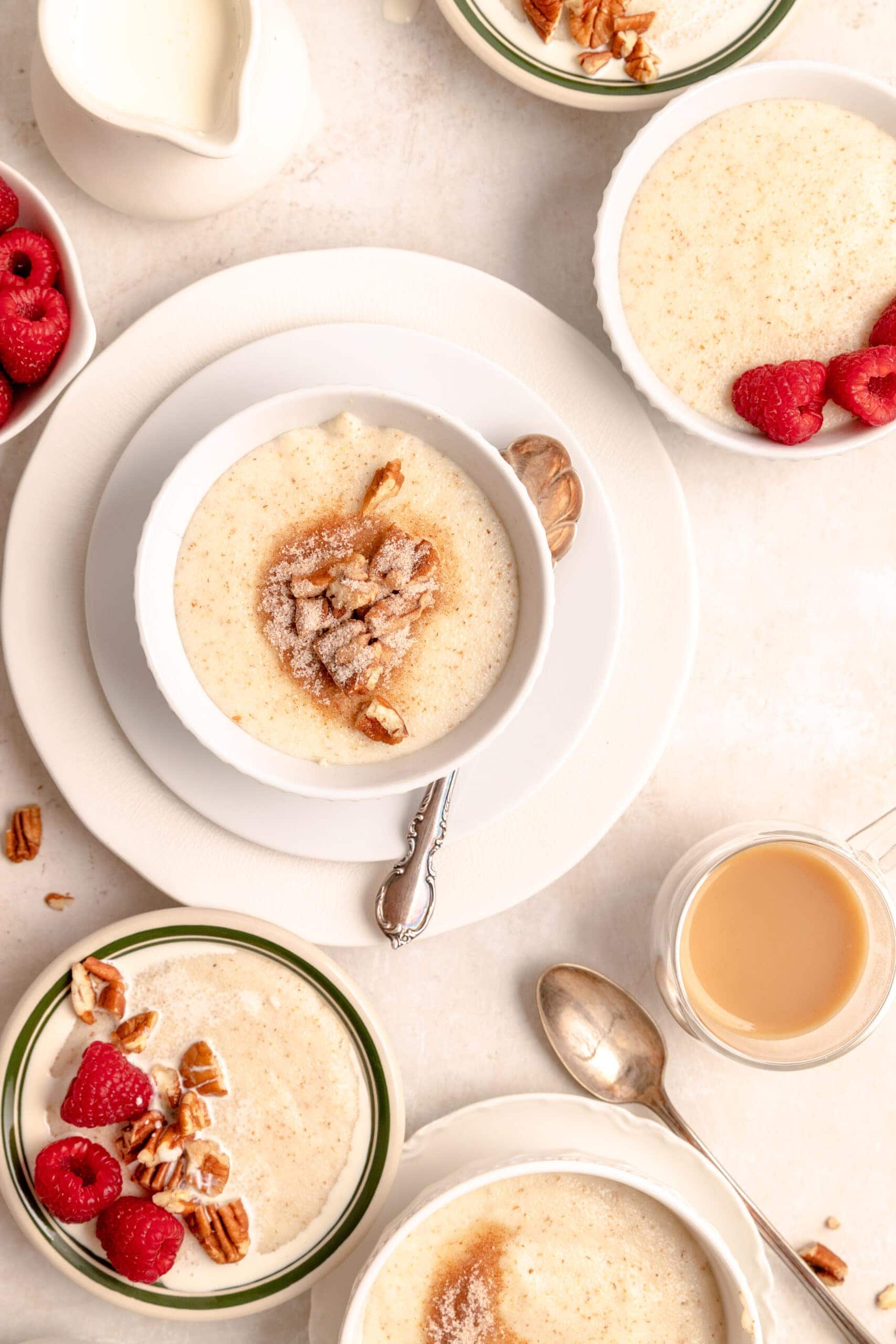 Overhead image of table with multiple bowls of Grießbrei topped with nuts, cinnamon sugar and raspberries.