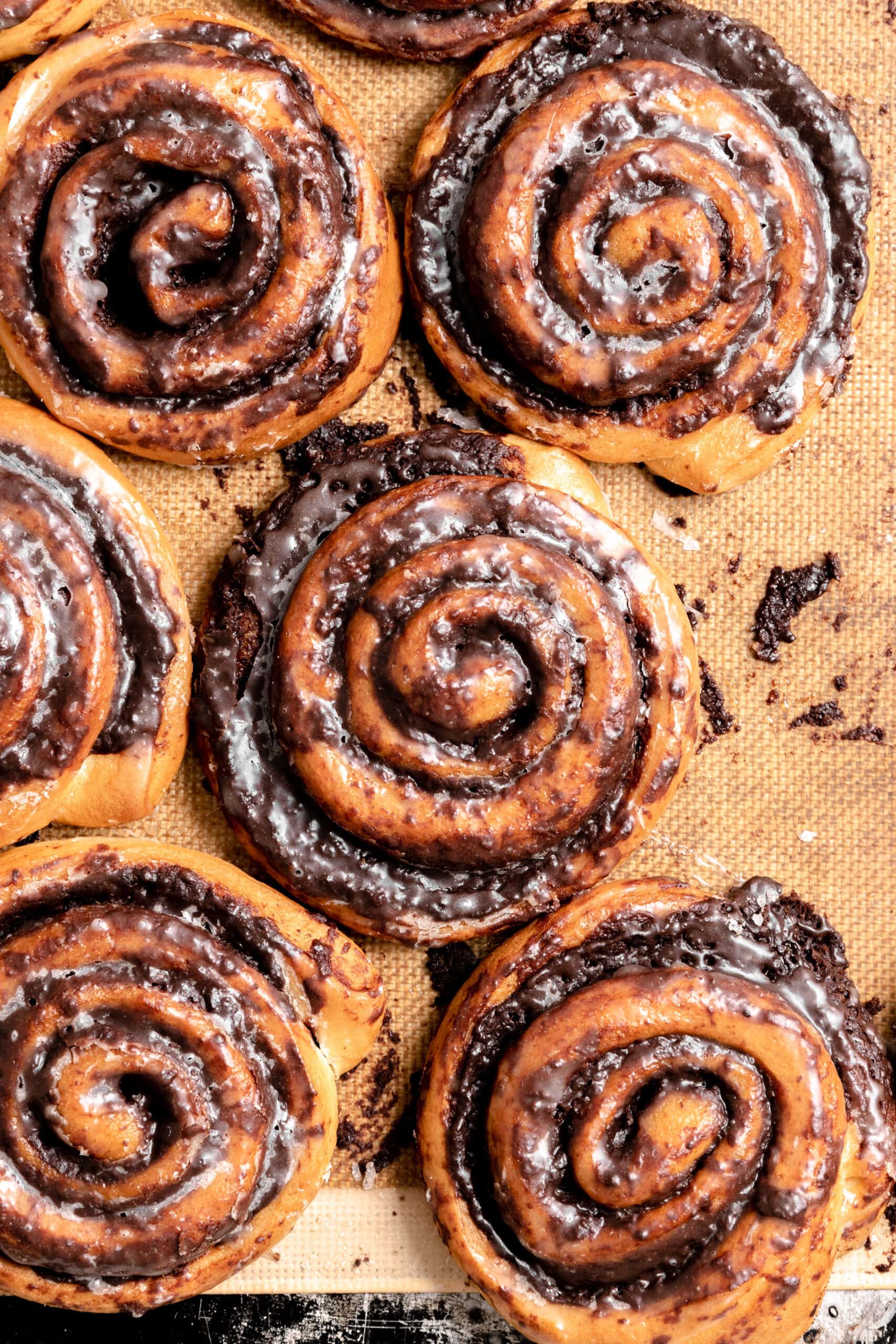 Overhead image of multiple schoko shcnecken/ chocolate pinwheels, side by side on a silicone baking mat.