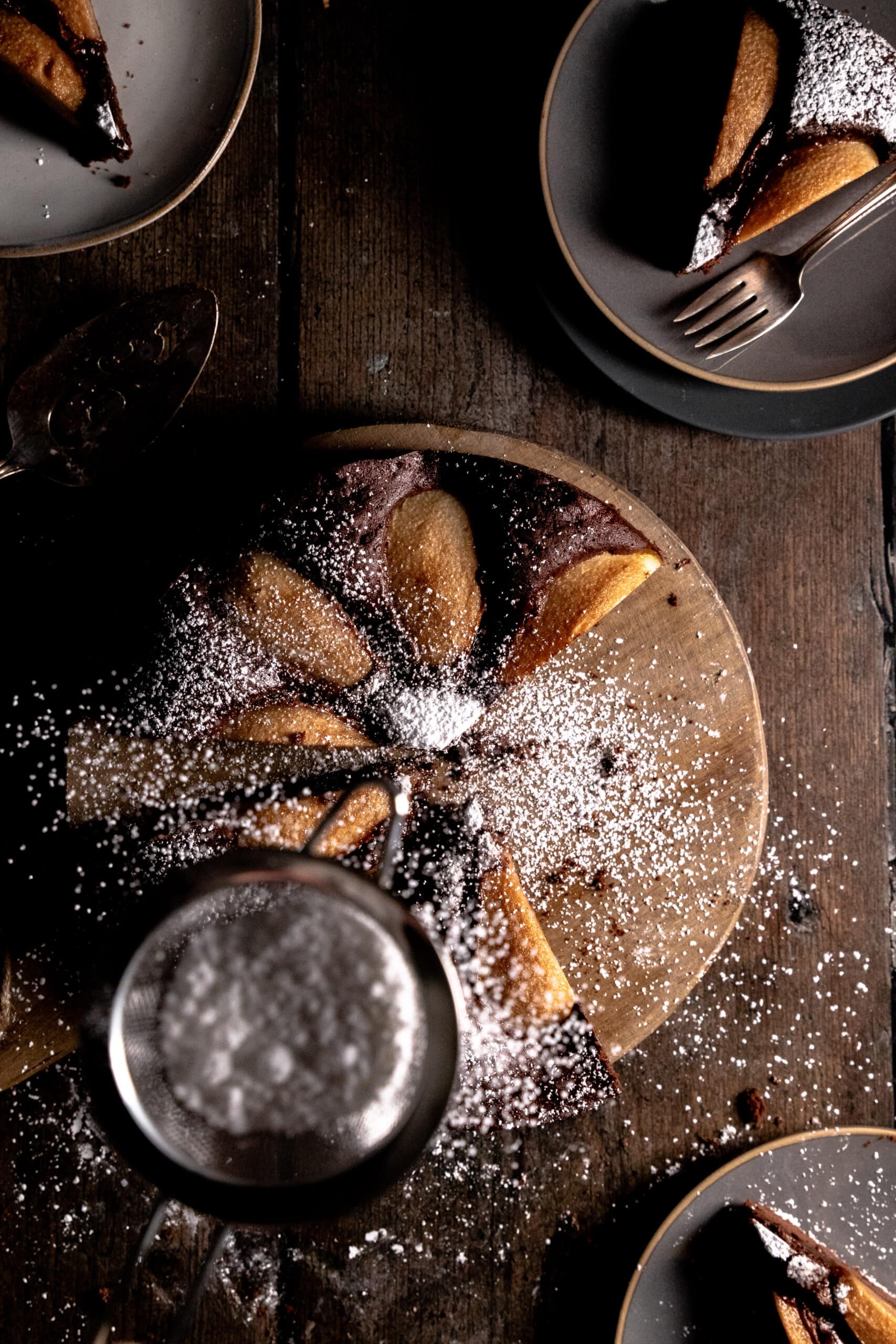Overhead view of chocolate pear cake being dusted with powdered sugar.