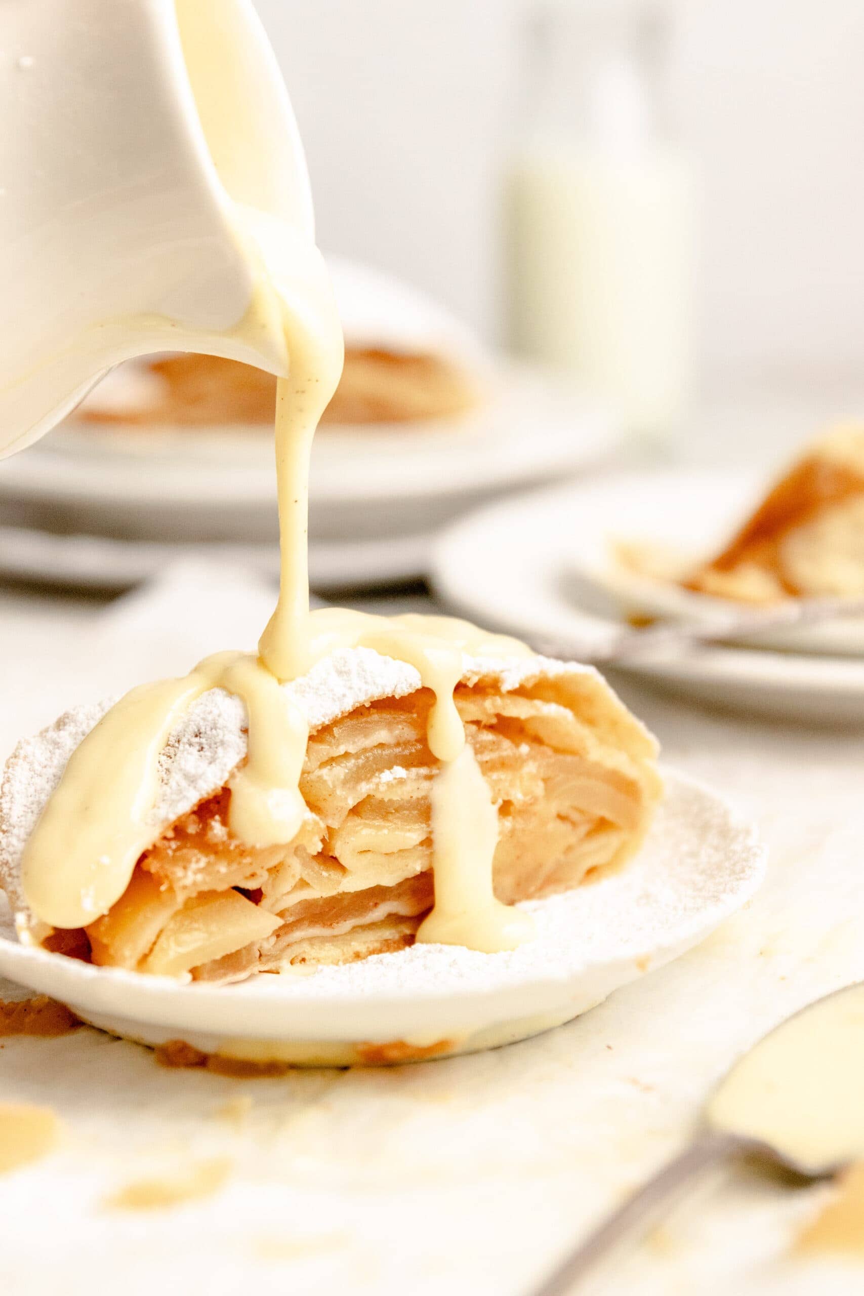 Side view of a slice of easy apple strudel with vanille soße being poured on top.