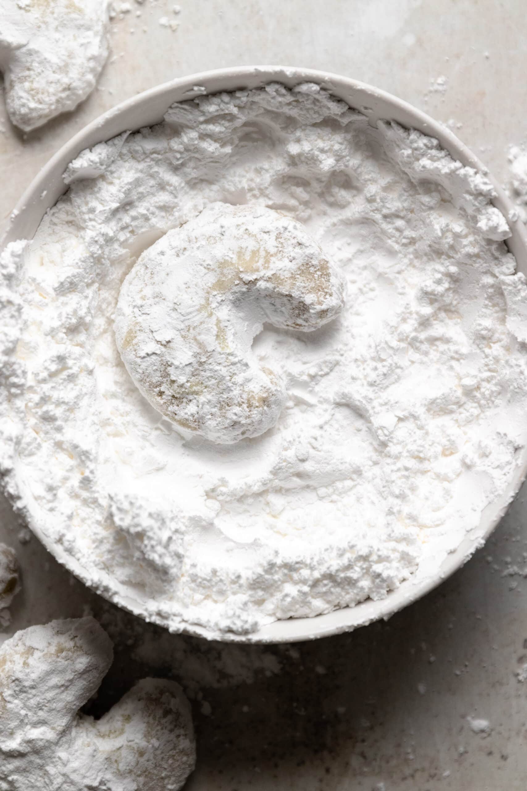 Overhead image of a Chai Kipferl cookie in a bowl of powdered sugar.