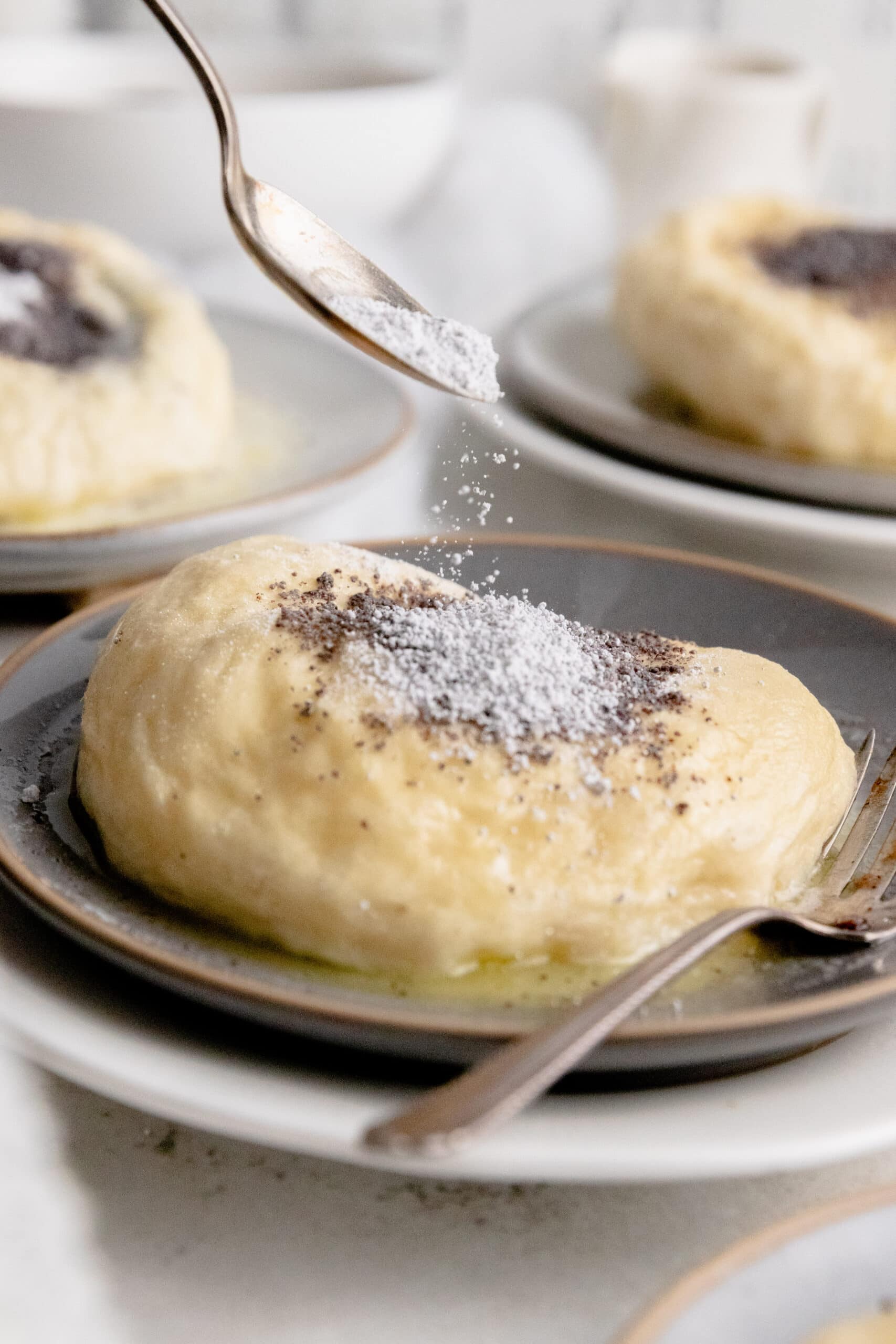 Side view of a germknödel being sprinkled with poppyseeds and powdered sugar.