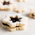 Side view of linzer plätzchen on a white surface and dusted with powdered sugar.