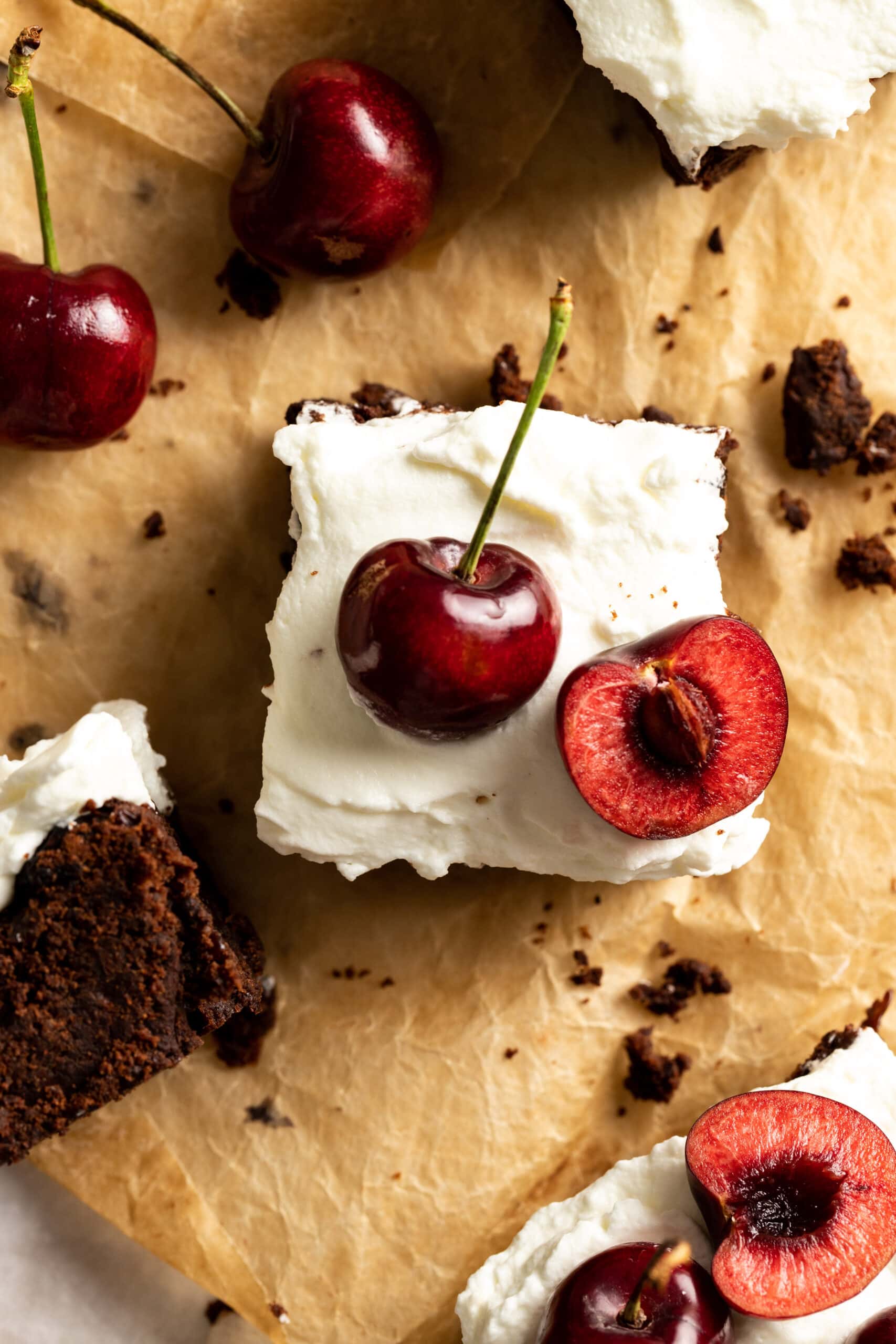 Overhead image of brownie squares topped with whipped cream and fresh cherries on top.