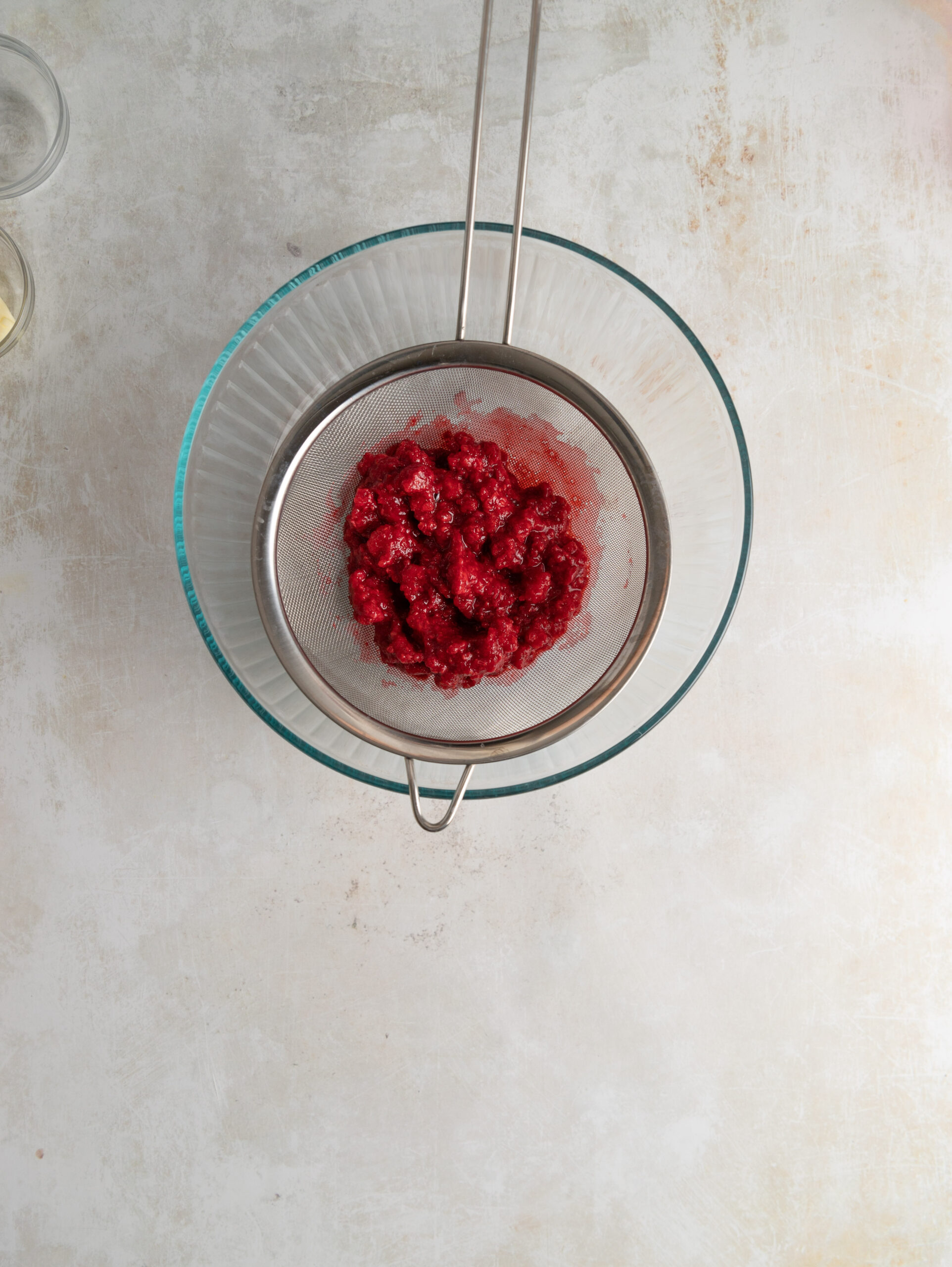 Frozen raspberries in a sieve draining over a bowl.