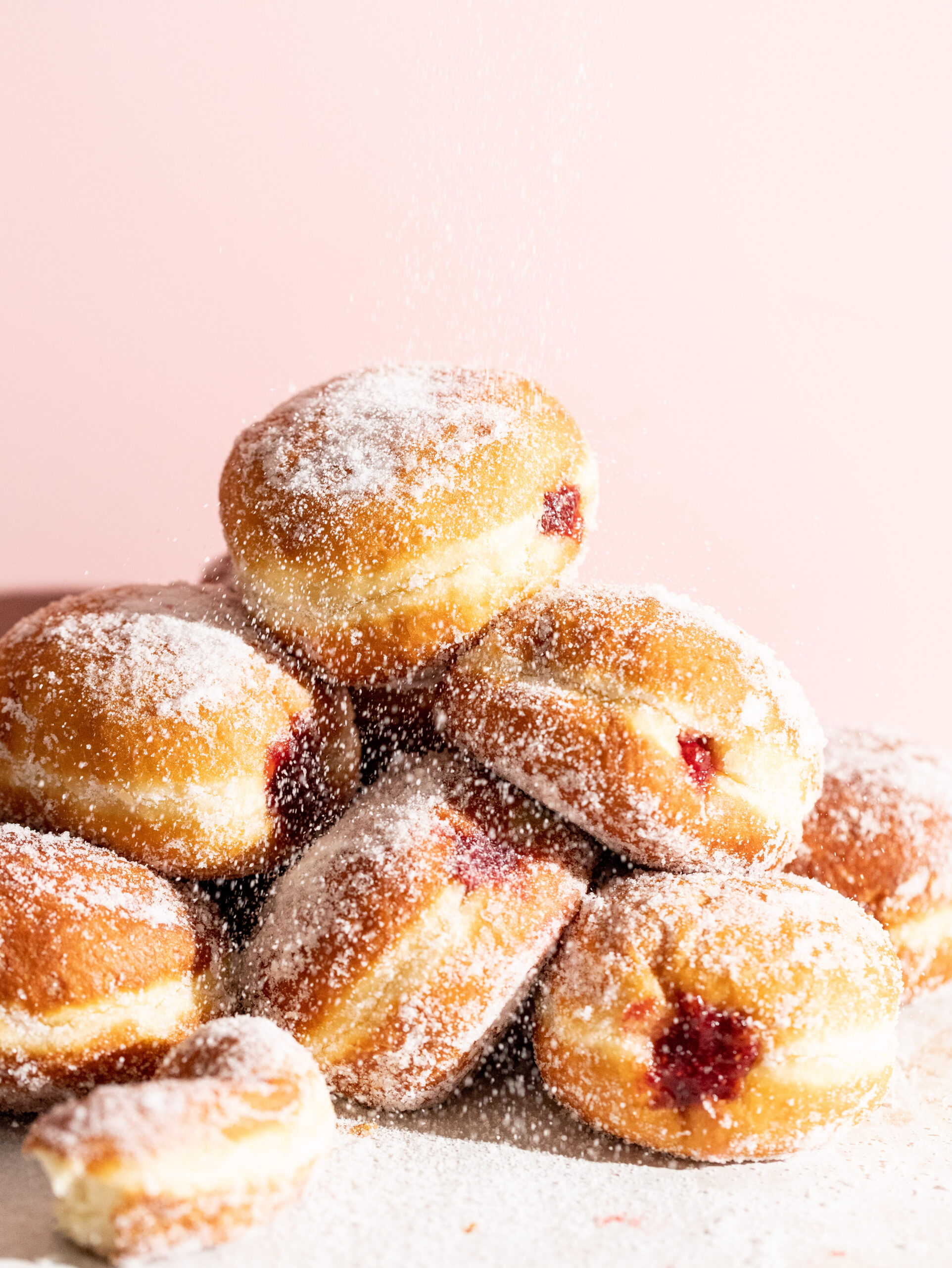 Side view of a pile of jam filled krapfen with sugar being poured over top.