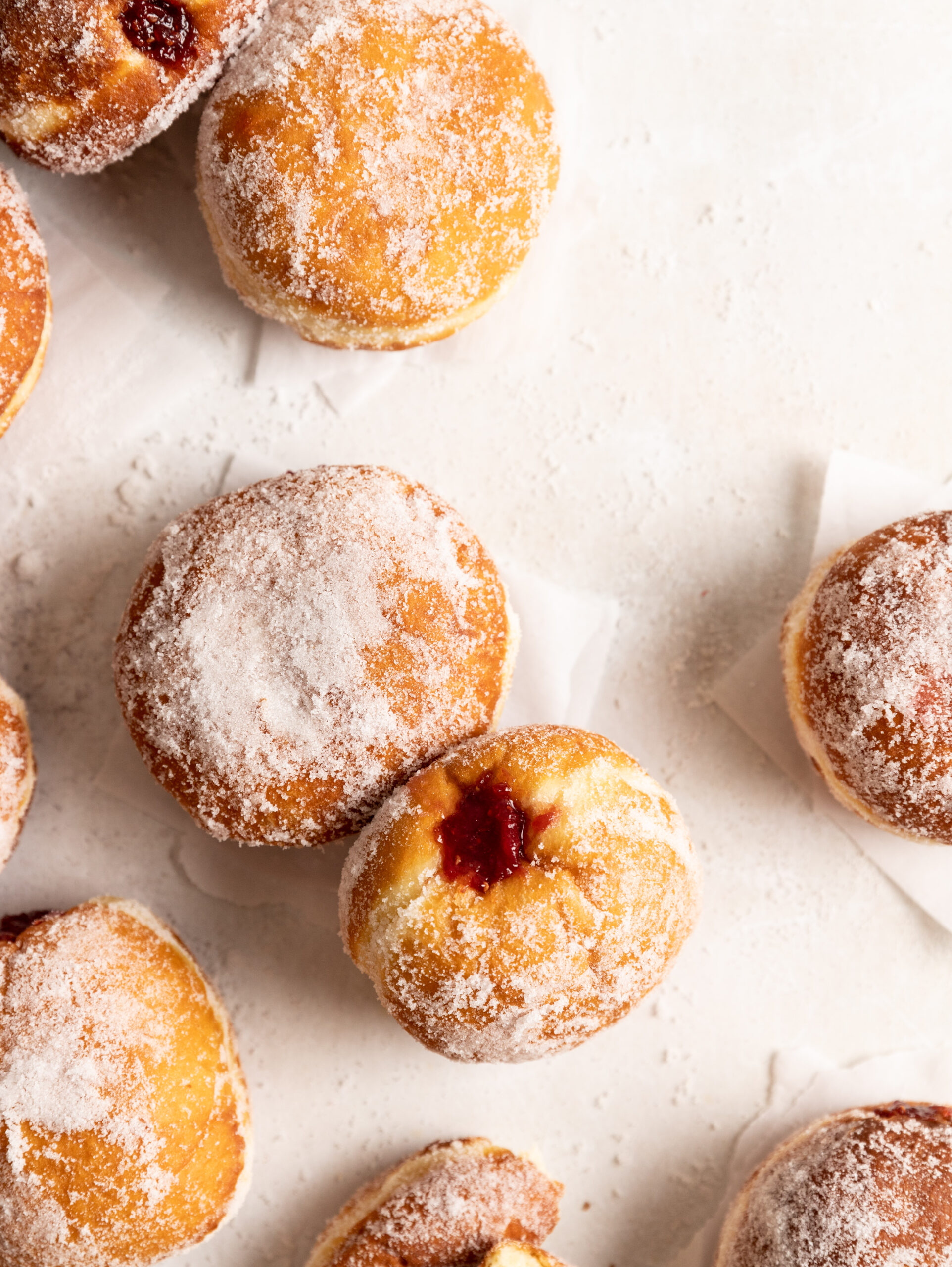 Overhead image of multiple jam filled krapfen rolled in sugar on a few squares of parchment paper.