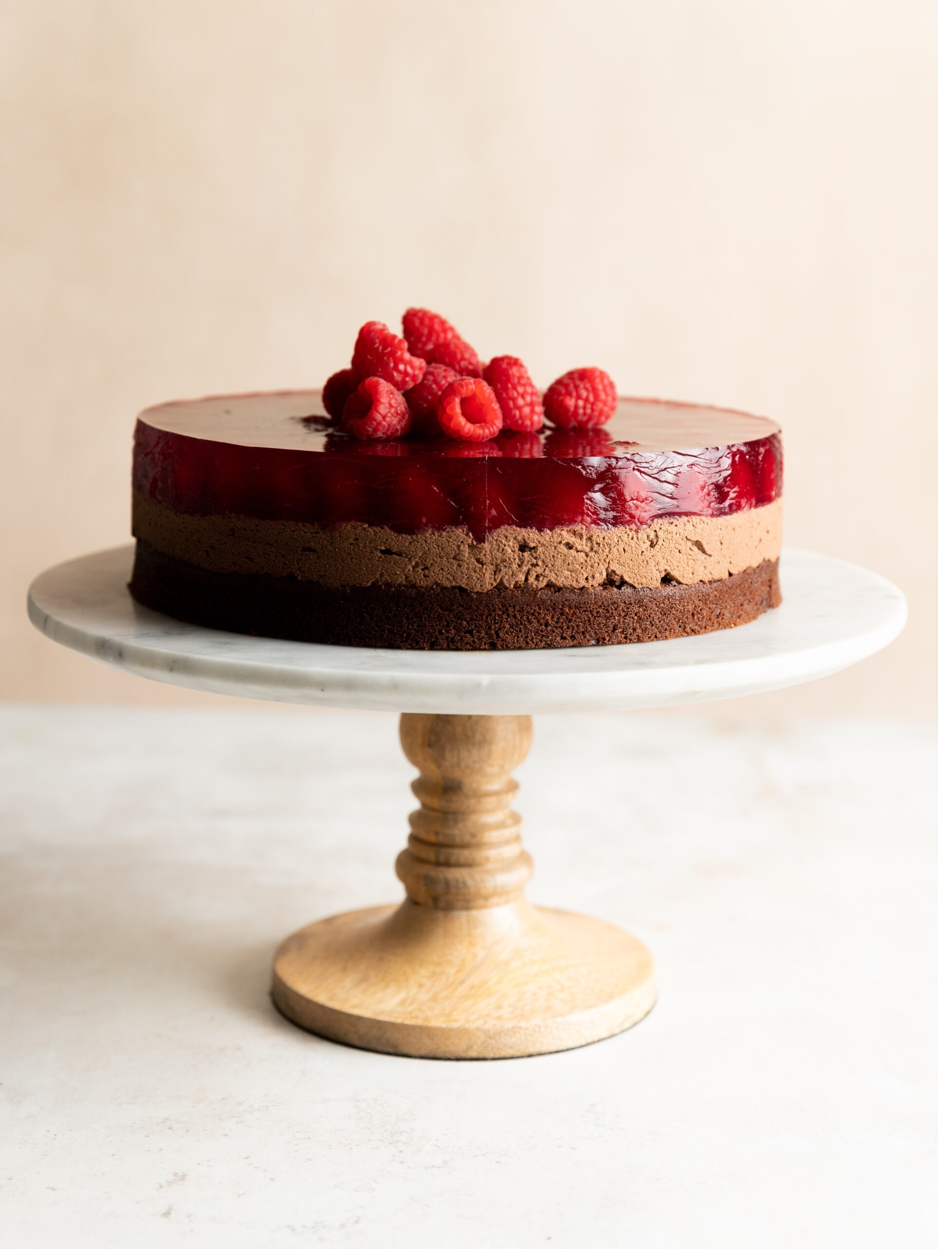 Side view of Schoko Himbeerkuchen topped with fresh raspberries on a marble and wood cake stand.