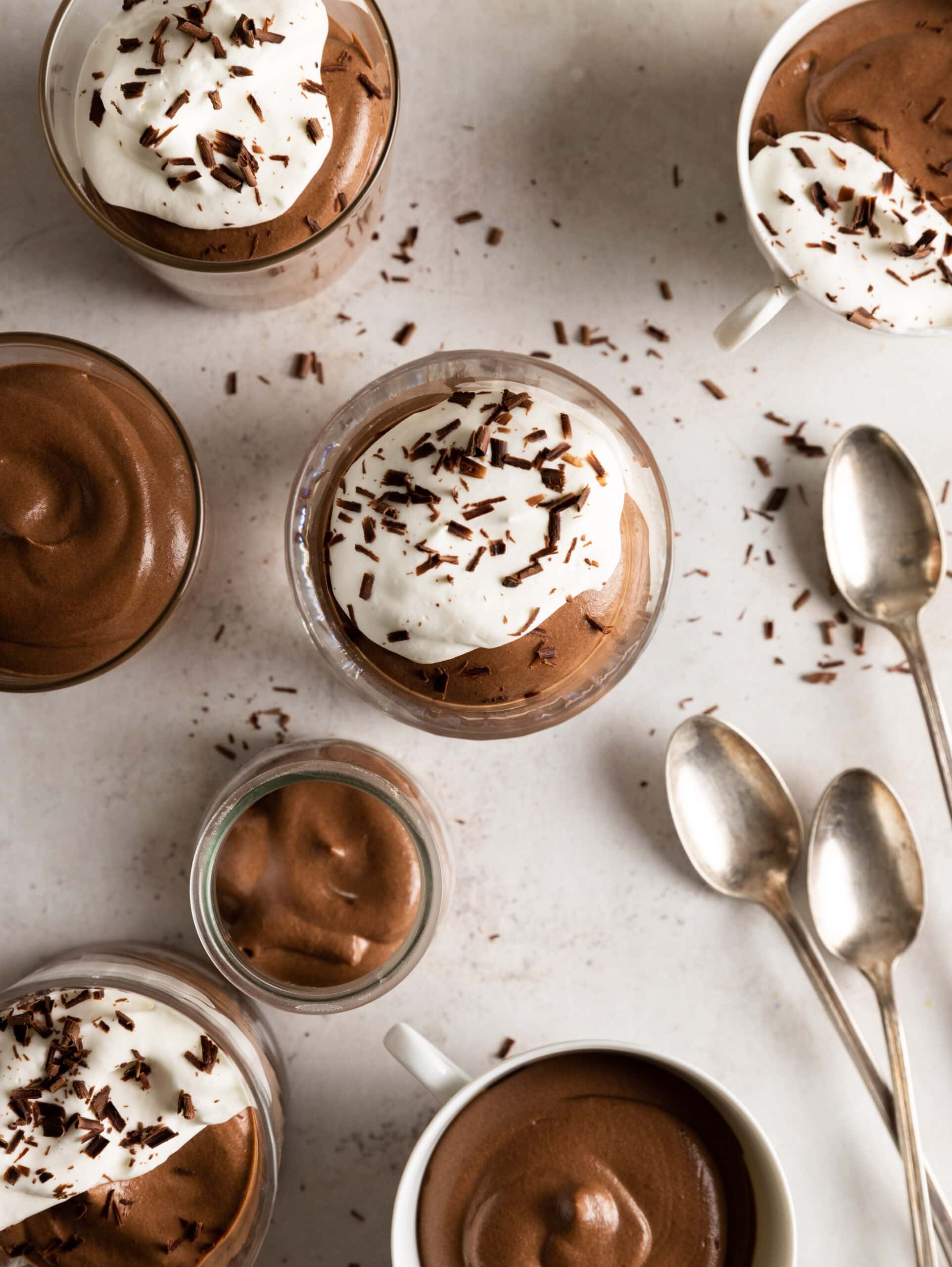 Overhead image of multiple glasses and cups of chocolate Bavarian cream and 3 spoons.