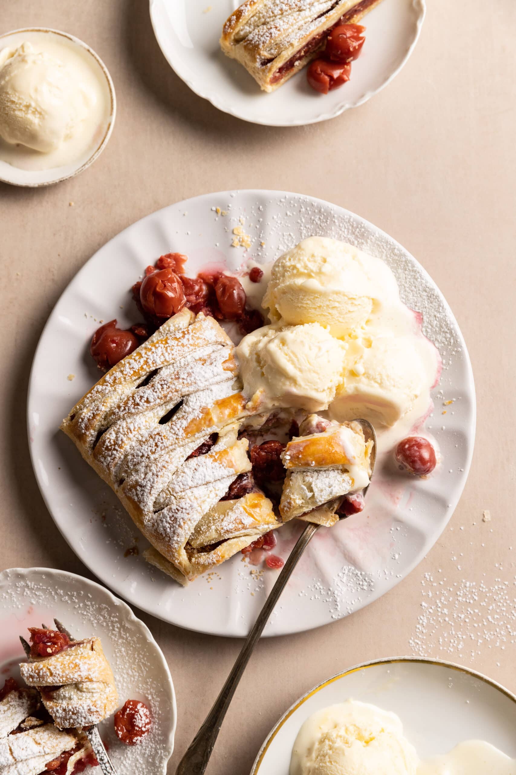 Overhead view of a large piece of cherry strudel on a white plate with 3 scoops of vanilla ice cream. 