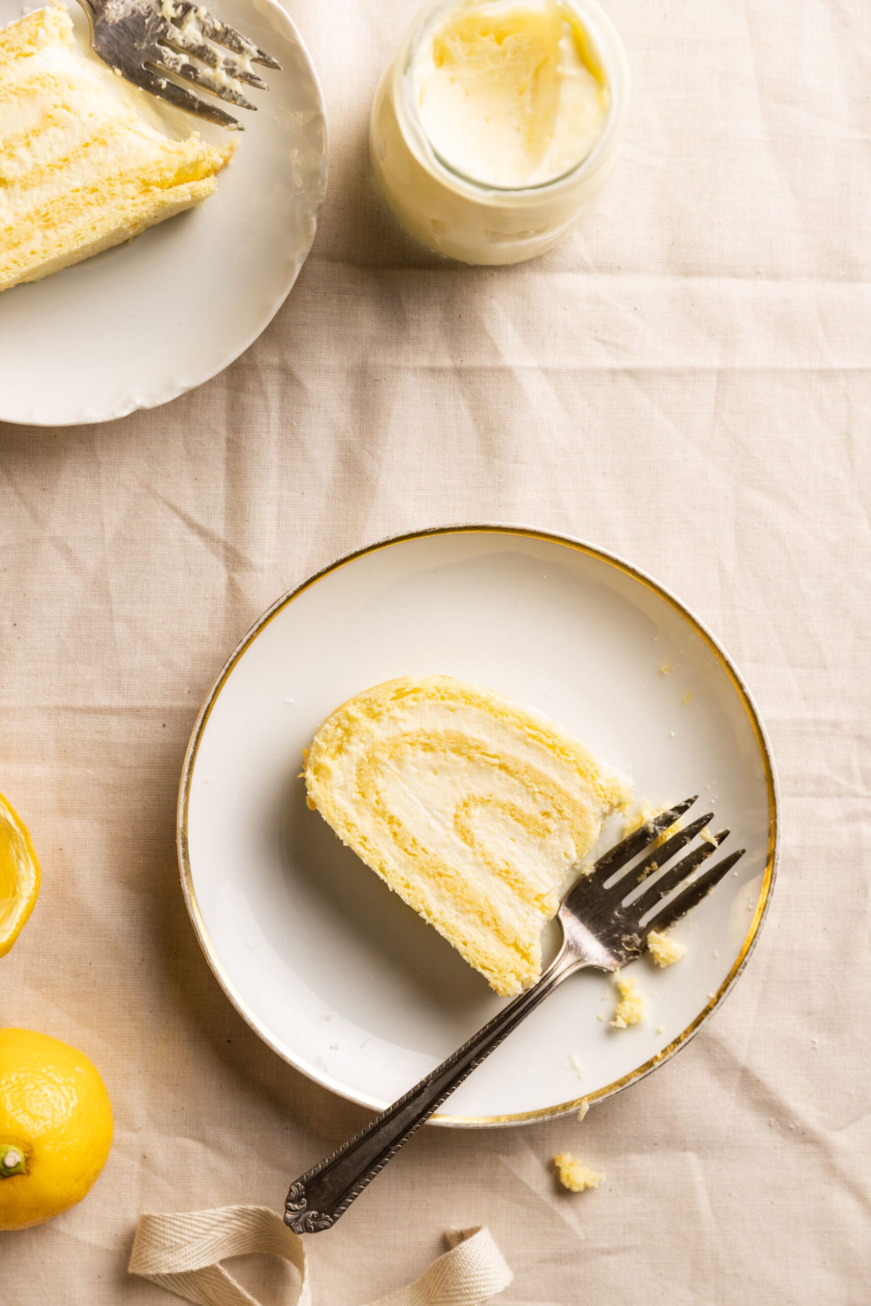Overhead view of two white plates, each with a slice of lemon roulade on them and a fork with a bite taken out. 
