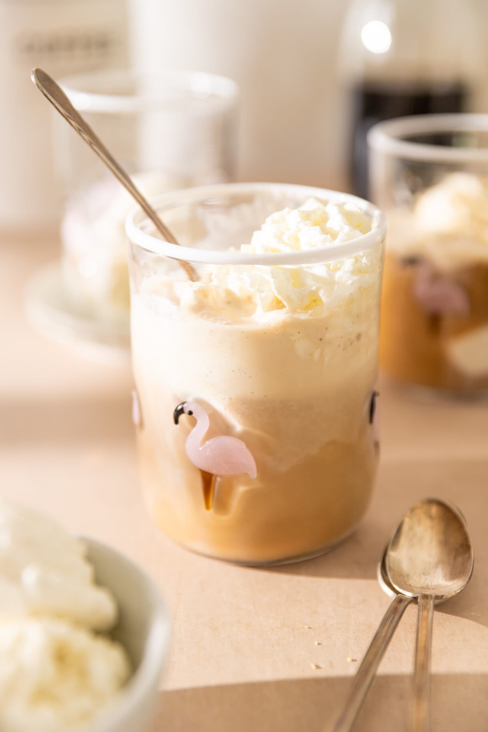 Side view of a clear glass filled with coffee, vanilla ice cream, and topped with whipped cream.
