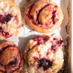 Overhead image of six cherry sweet rolls on a parchment lined baking sheet.