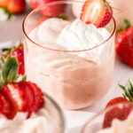 Side view of a pink glass filled with strawberry bavarian cream, topped with whipped cream and a fresh strawberry half.