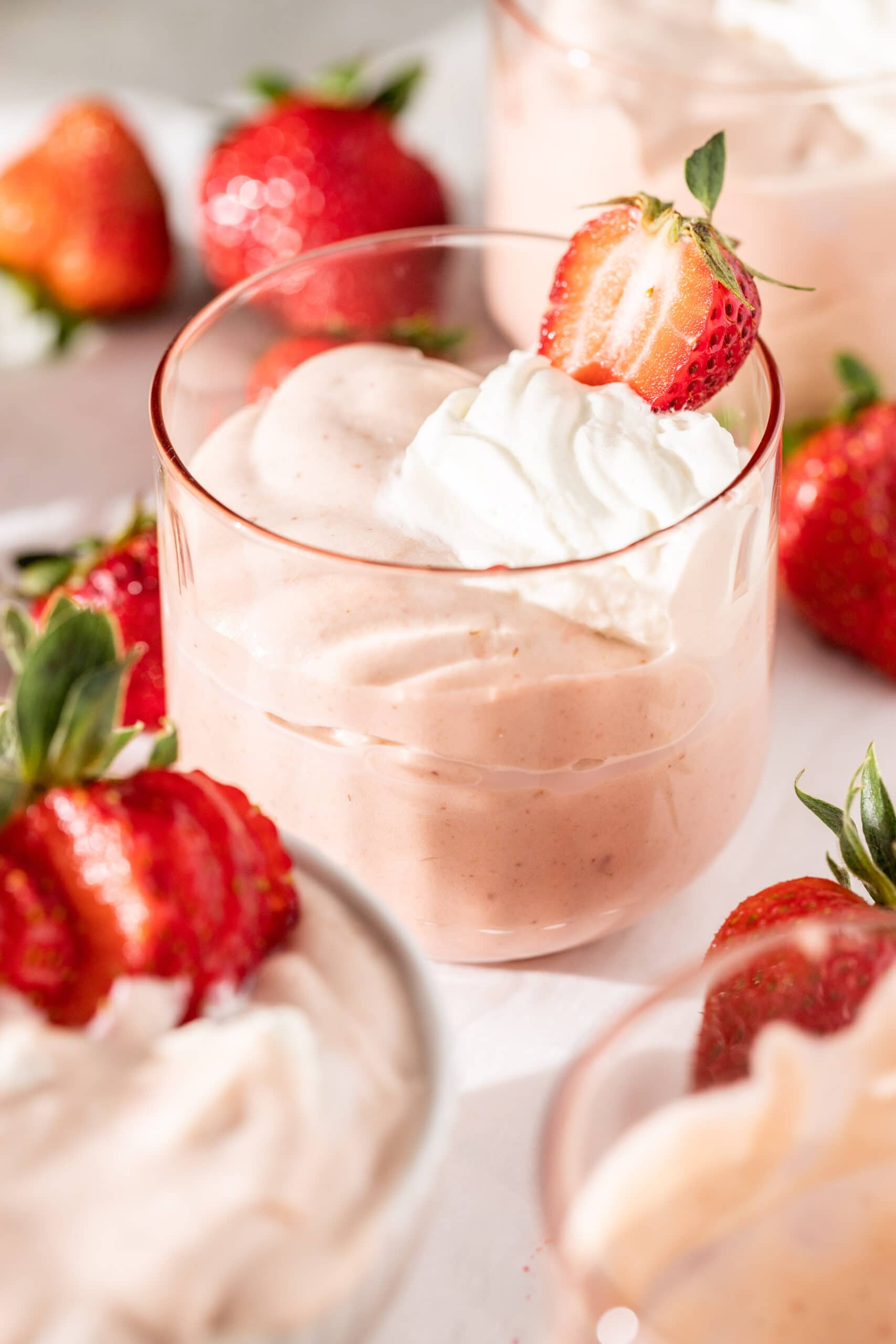 Side view of a pink glass filled with strawberry bavarian cream, topped with whipped cream and a fresh strawberry half.