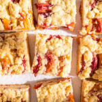 Overhead view of multiple square slices of peach streusel on a piece of white parchment paper.