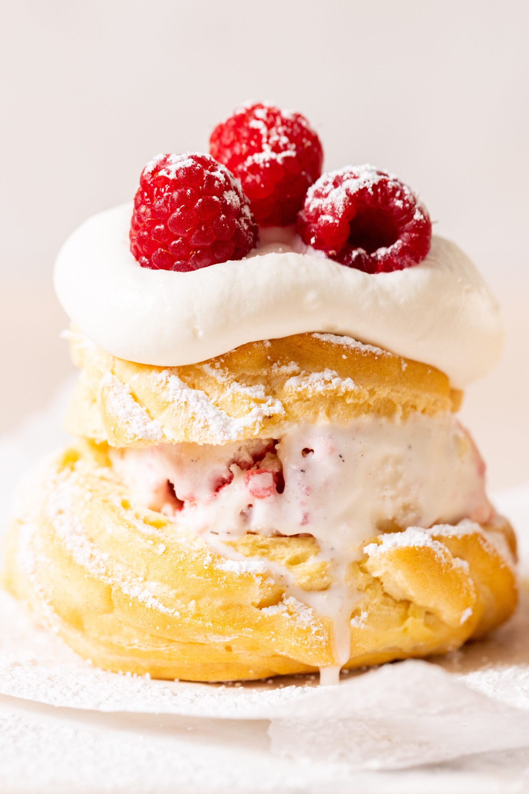 Side view of a windbeutel filled with ice cream, topped with whipped cream and raspberries.