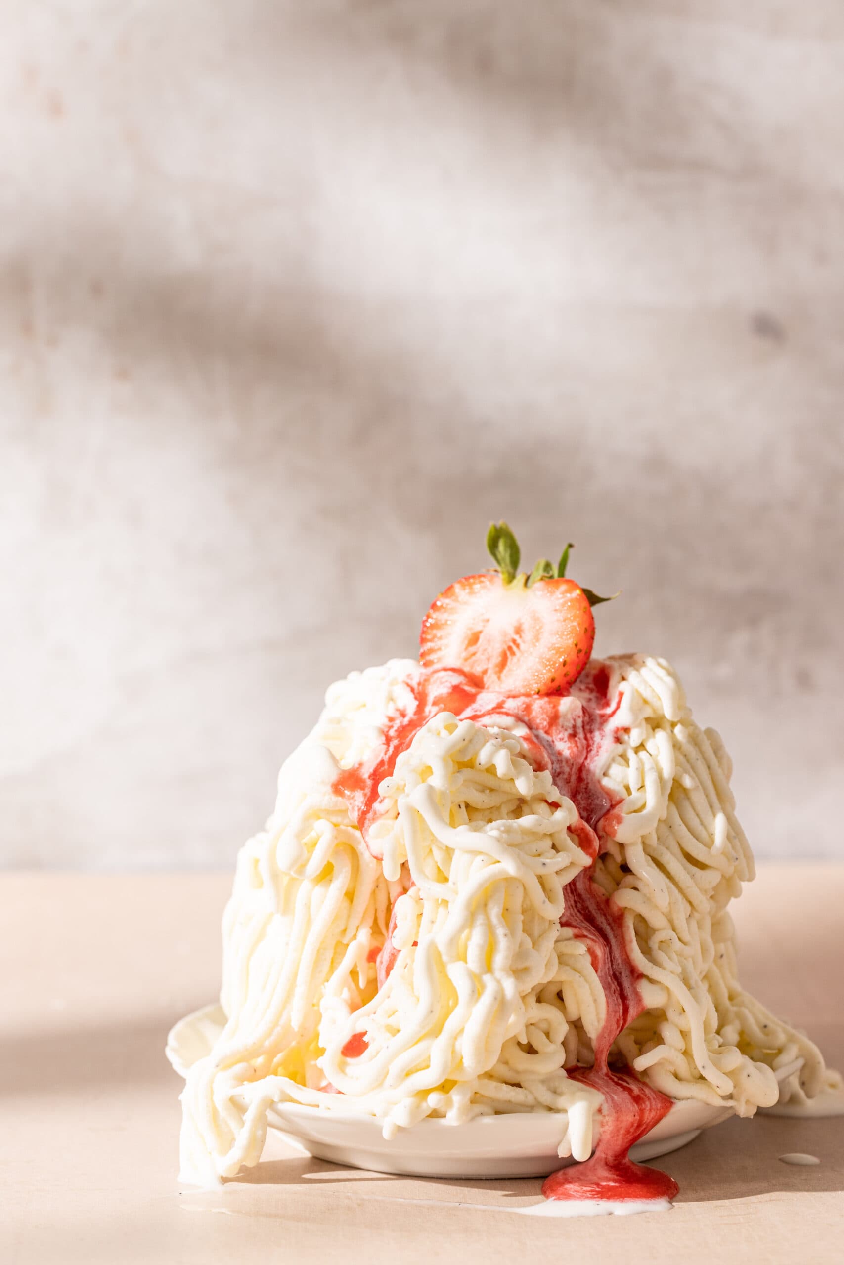 Pile of spaghettieis topped with strawberry sauce and a fresh strawberry.