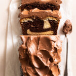 Overhead view of a marble loaf cake with whipped chocolate ganache cut into slices so that the internal swirl is visible.