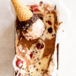 Overhead view of a black forest ice cream in a loaf pan with a scoop on an ice cream cone.