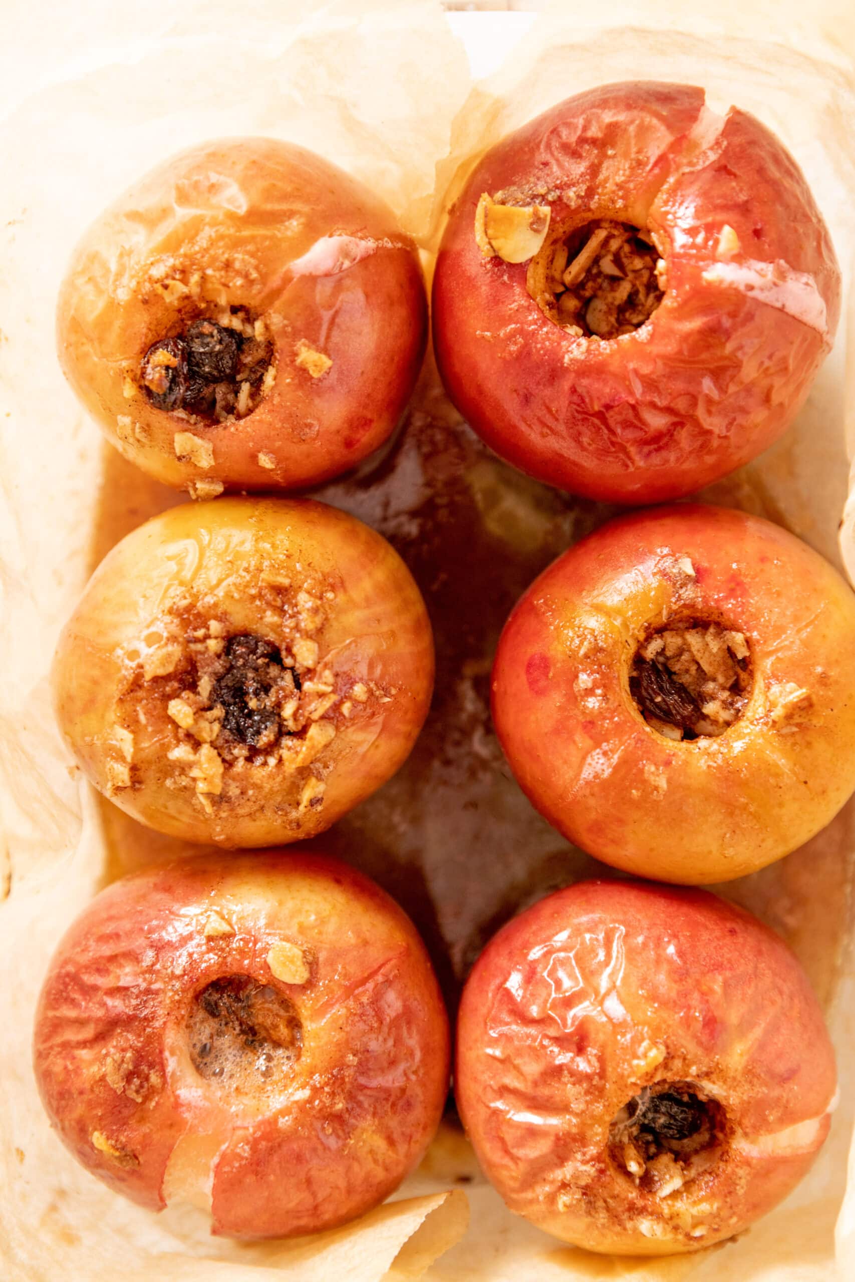 Baking dish lined with parchment paper with 6 filled and baked apples. 