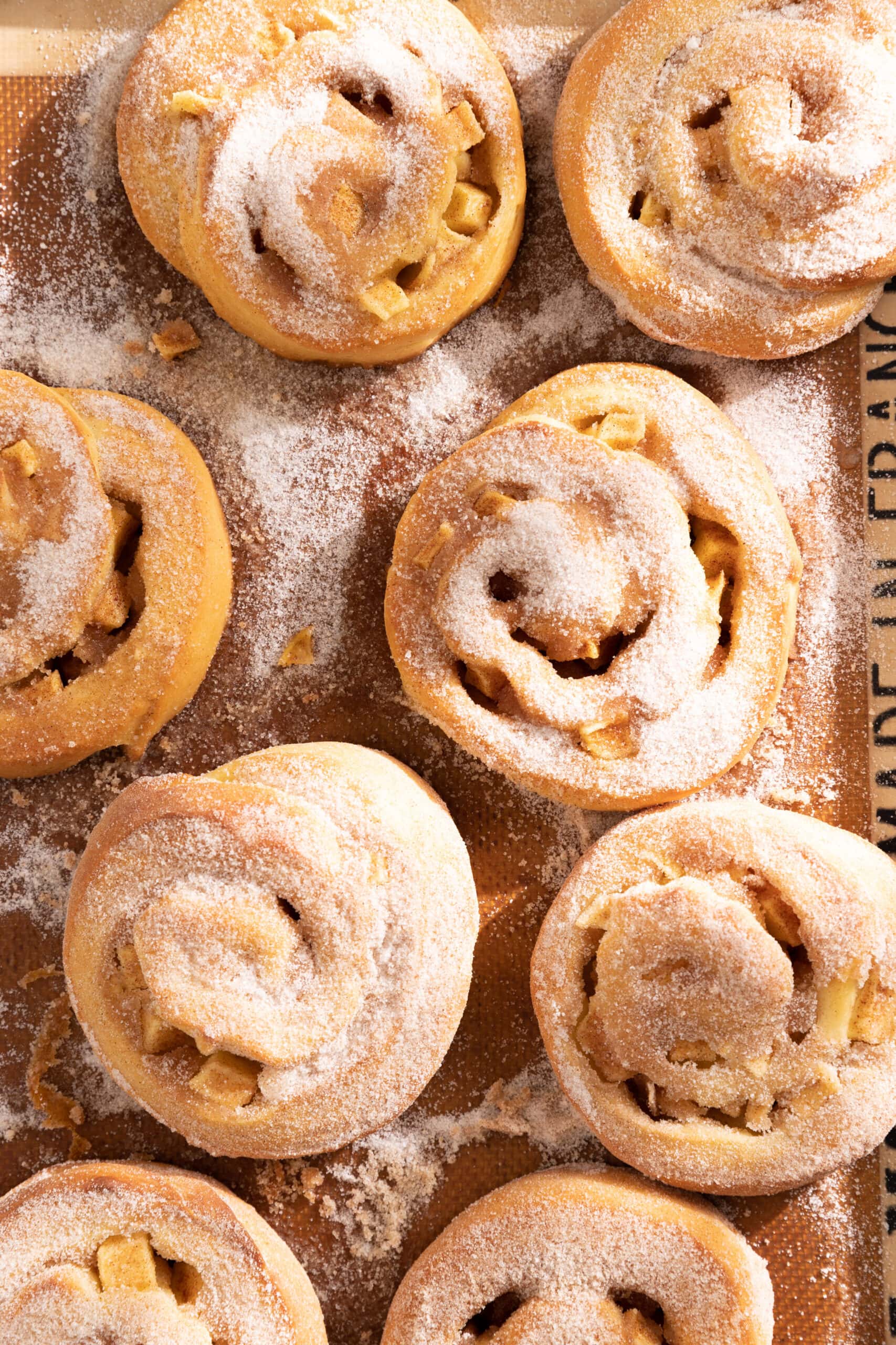 Overhead view of freshly baked apple cinnamon rolls on a silicone baking mat topped with cinnamon sugar.