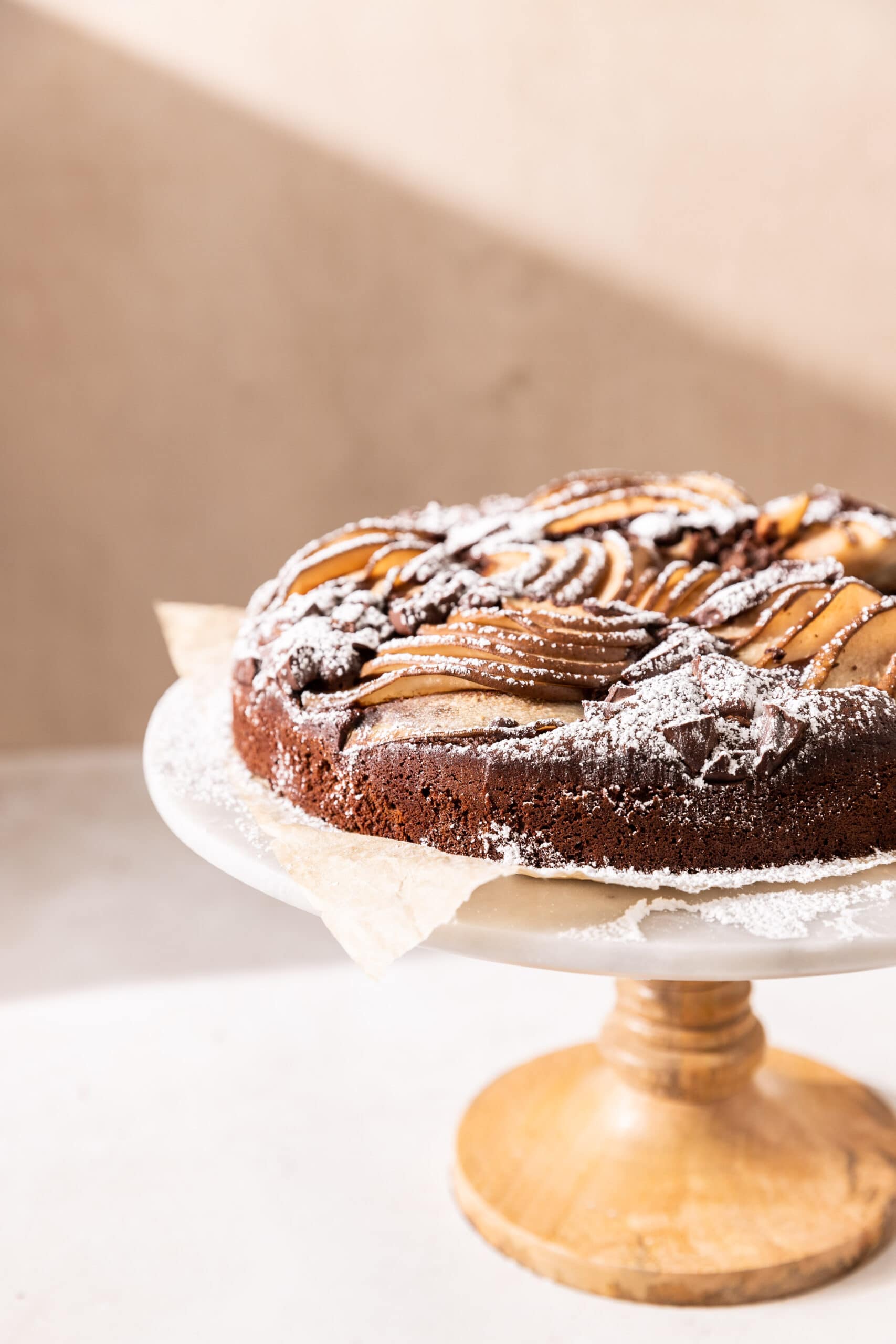 Side view of a chocolate pear cake on a cake stand dusted with powdered sugar. 
