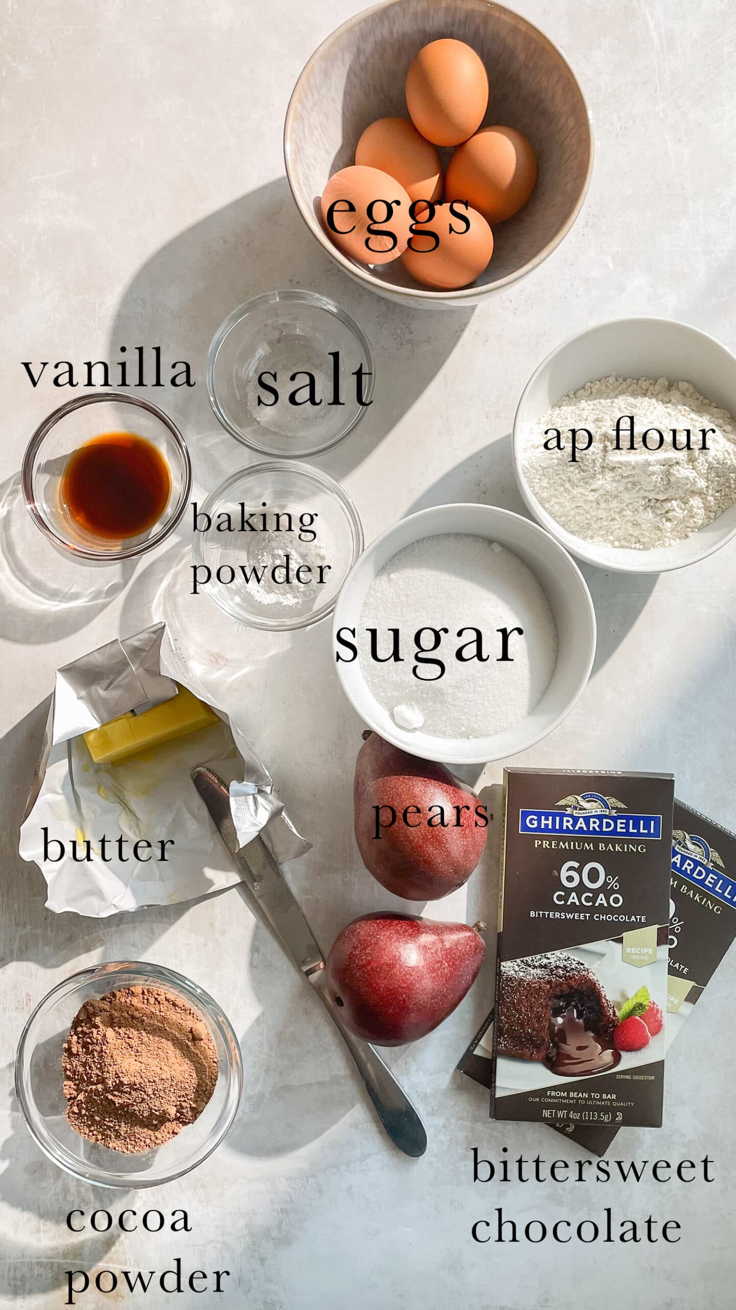 Ingredients for chocolate pear cake laid out and labeled on a table. 