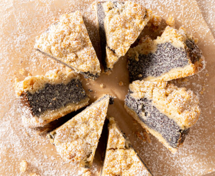 Overhead view of a mohnkuchen cut into slices, dusted with powdered sugar, with some tipped over to show the poppyseed layer.