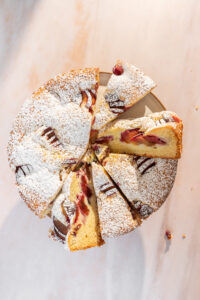 Overhead view of a plum cake, dusted with powdered sugar and cut into slices.