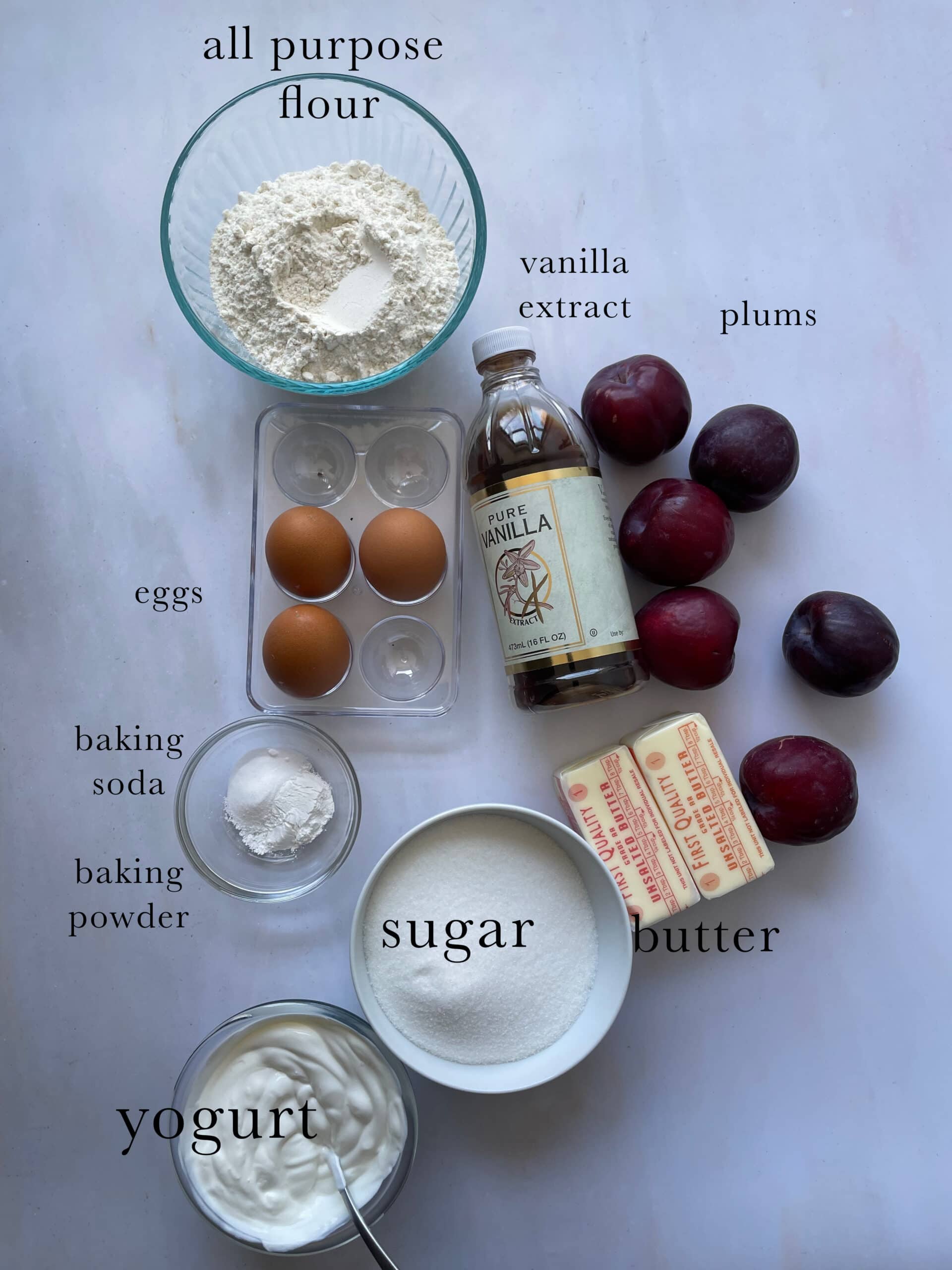 Ingredients needed for a plum cake labeled on a table.