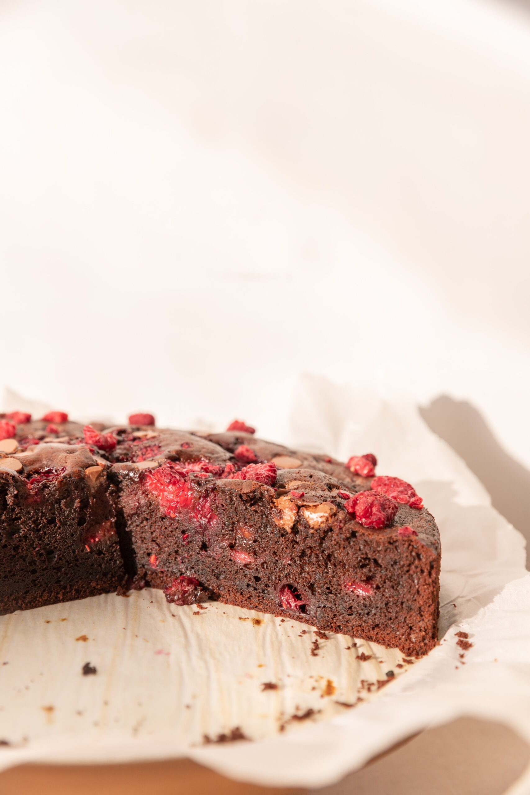 Easy Chocolate Raspberry Cake on a cake stand with parchment paper, cut into so the inside is visible. 