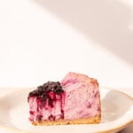 Side view of a slice of lemon blueberry cheesecake on a white ceramic plate.