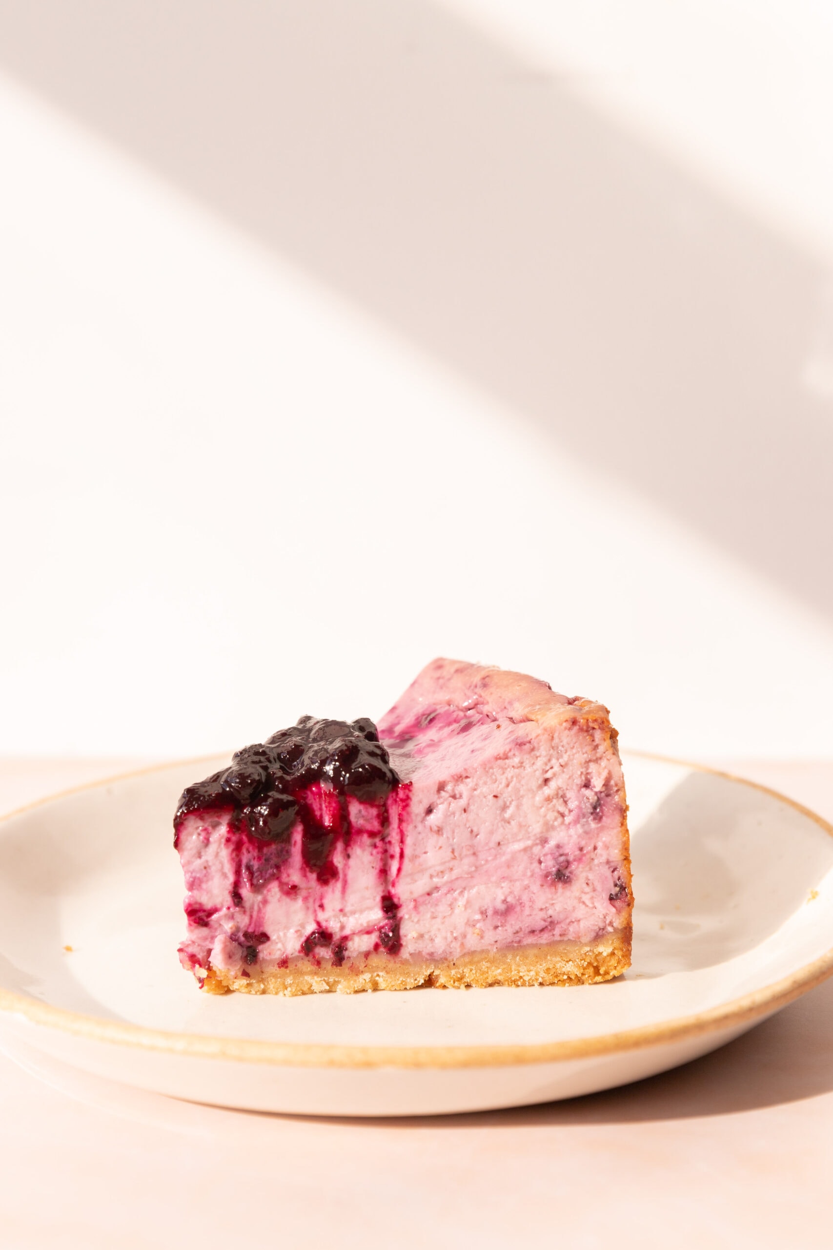 Side view of a slice of lemon blueberry cheesecake on a white ceramic plate. 