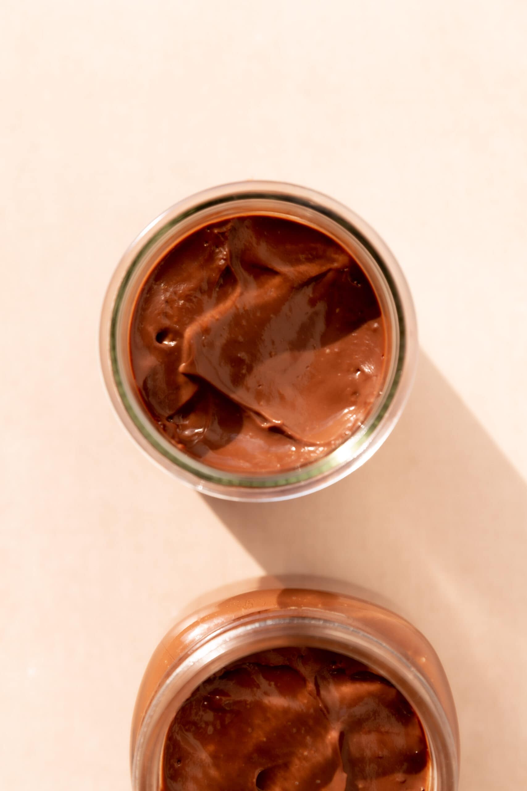 Overhead view of two little glass jars filled with creamy chocolate pudding.