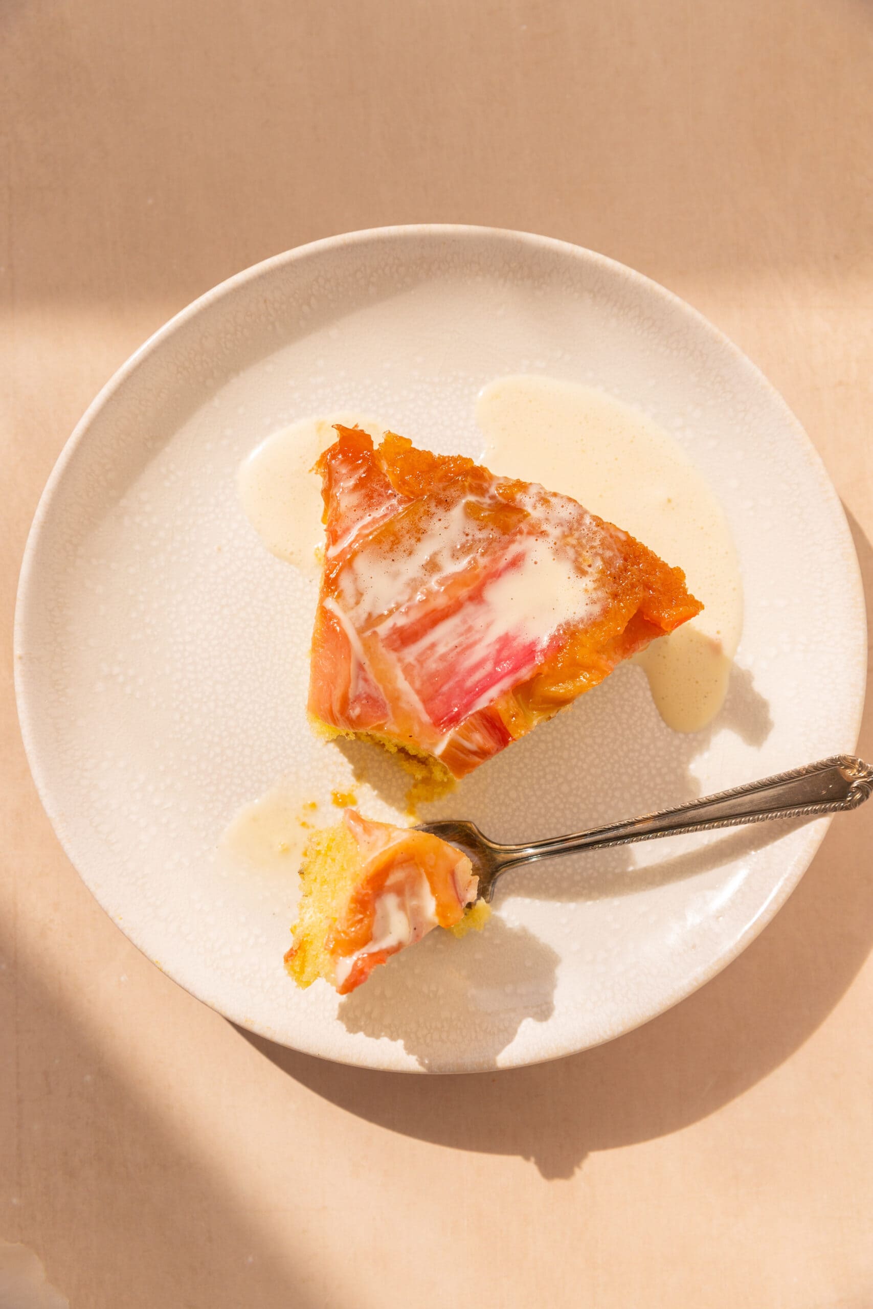 Overhead view of a slice of upside down rhubarb cake drizzled with a vanilla custard sauce. 