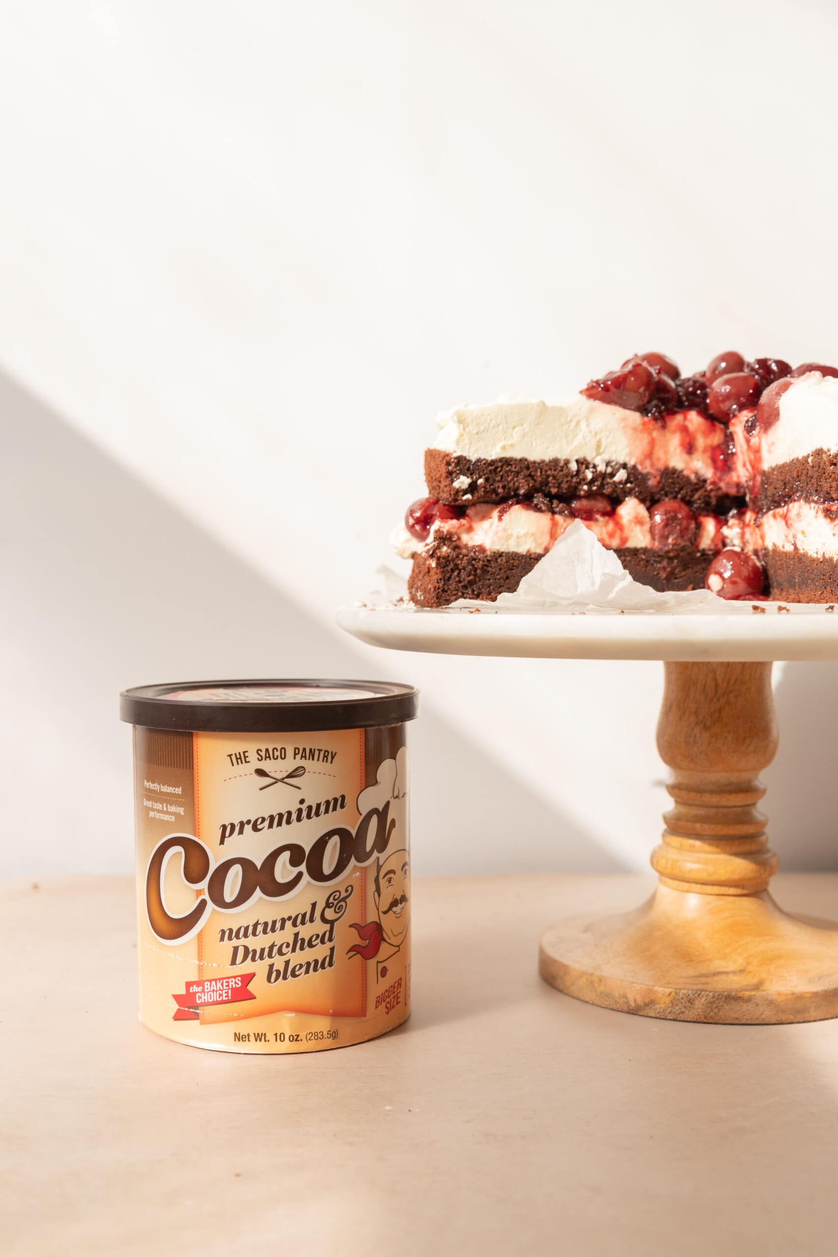 Image of Saco Cocoa powder container next to a cake stand with black forest cake on it.