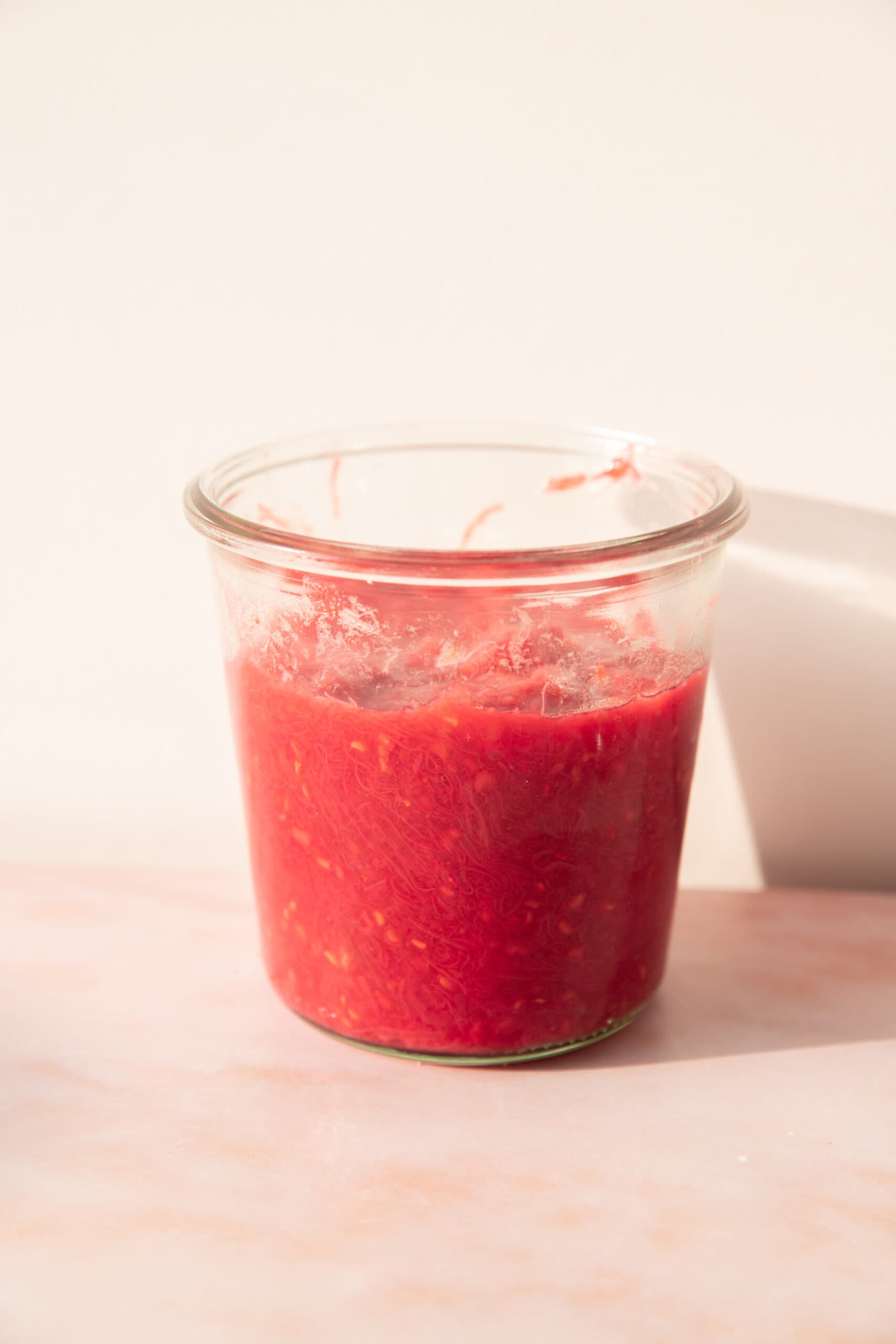 Side view of a glass jar filled with rhubarb compote.