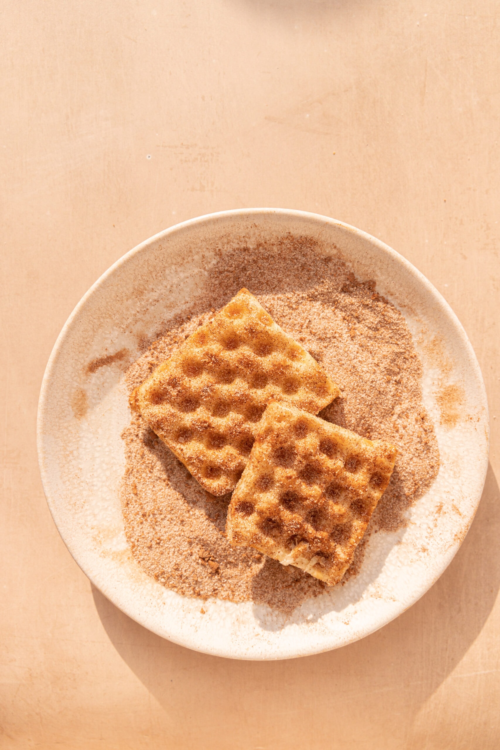 Overhead image of two puff pastry waffles on a plate with cinnamon sugar.
