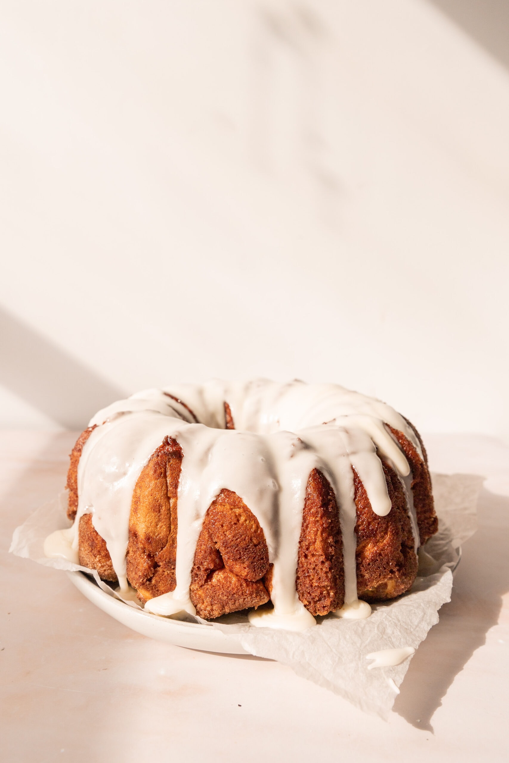 Side view of an iced cinnamon roll monkey bread on a parchment lined plate. 