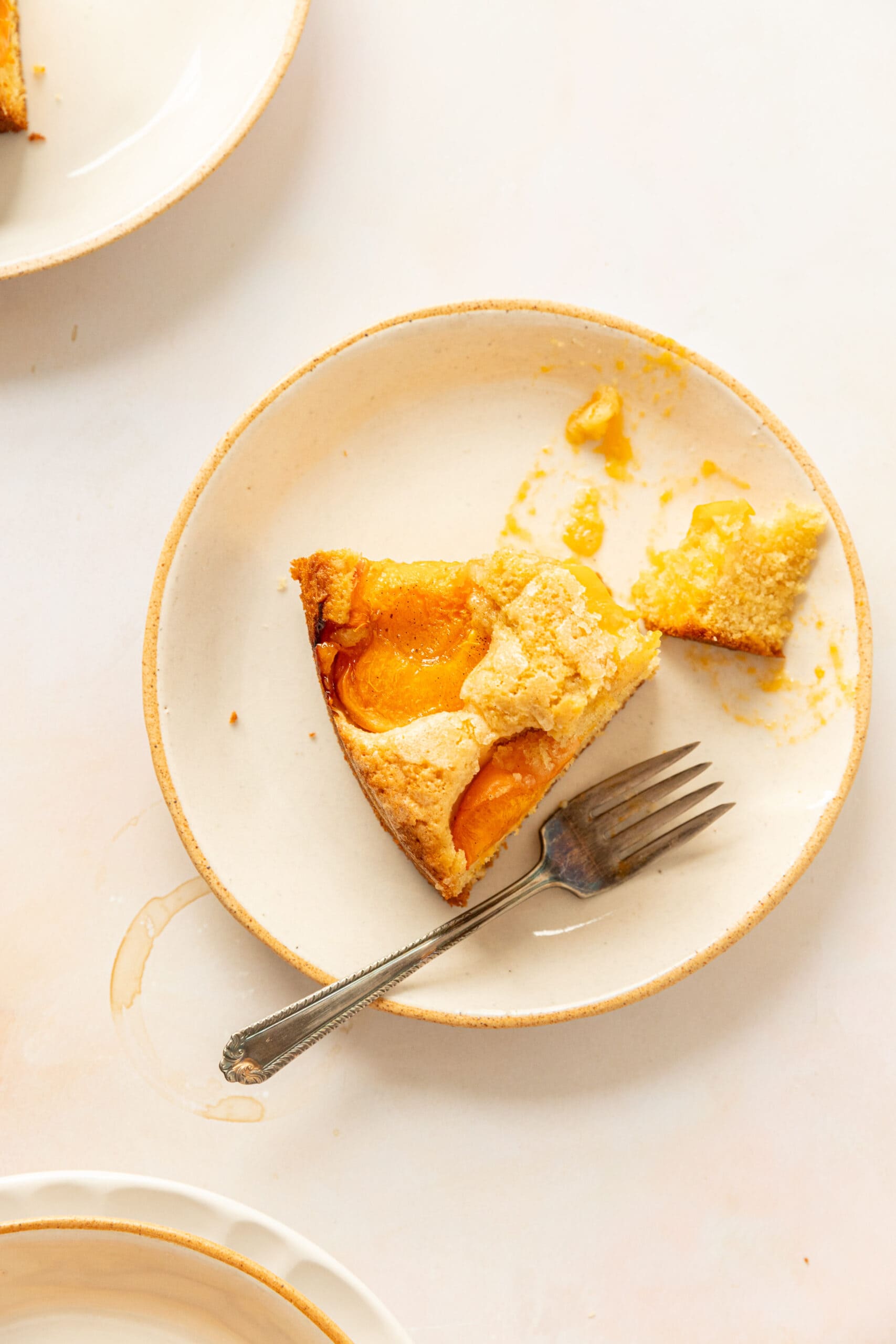 Slice of apricot cake on a white ceramic plate with a bite taken out of it. 