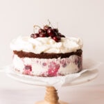 Side view of a black forest ice cream cake fully assembled on a cake stand lined with parchment paper.